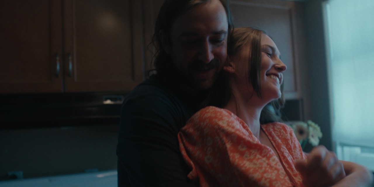 A couple embrace and smile beside a kitchen window