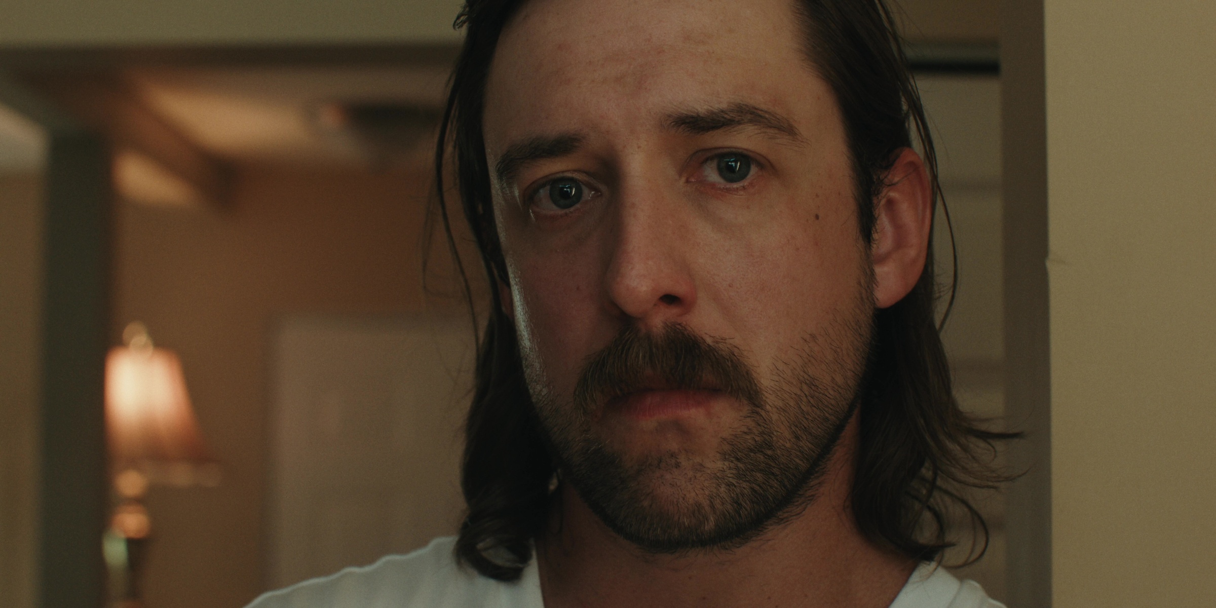 A bearded man looks ahead in a warmly lit kitchen — Bottom of the bottle