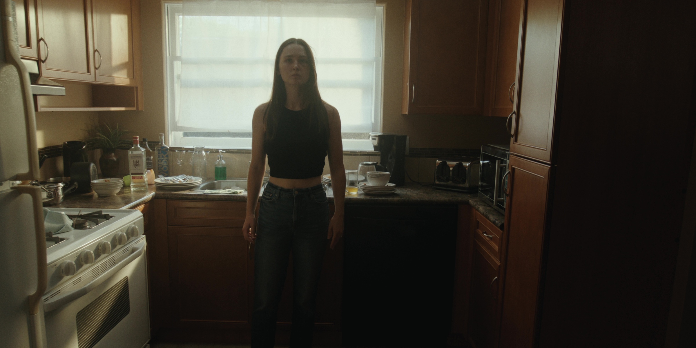 A woman stands alone in a sunlit kitchen — Bottom of the bottle