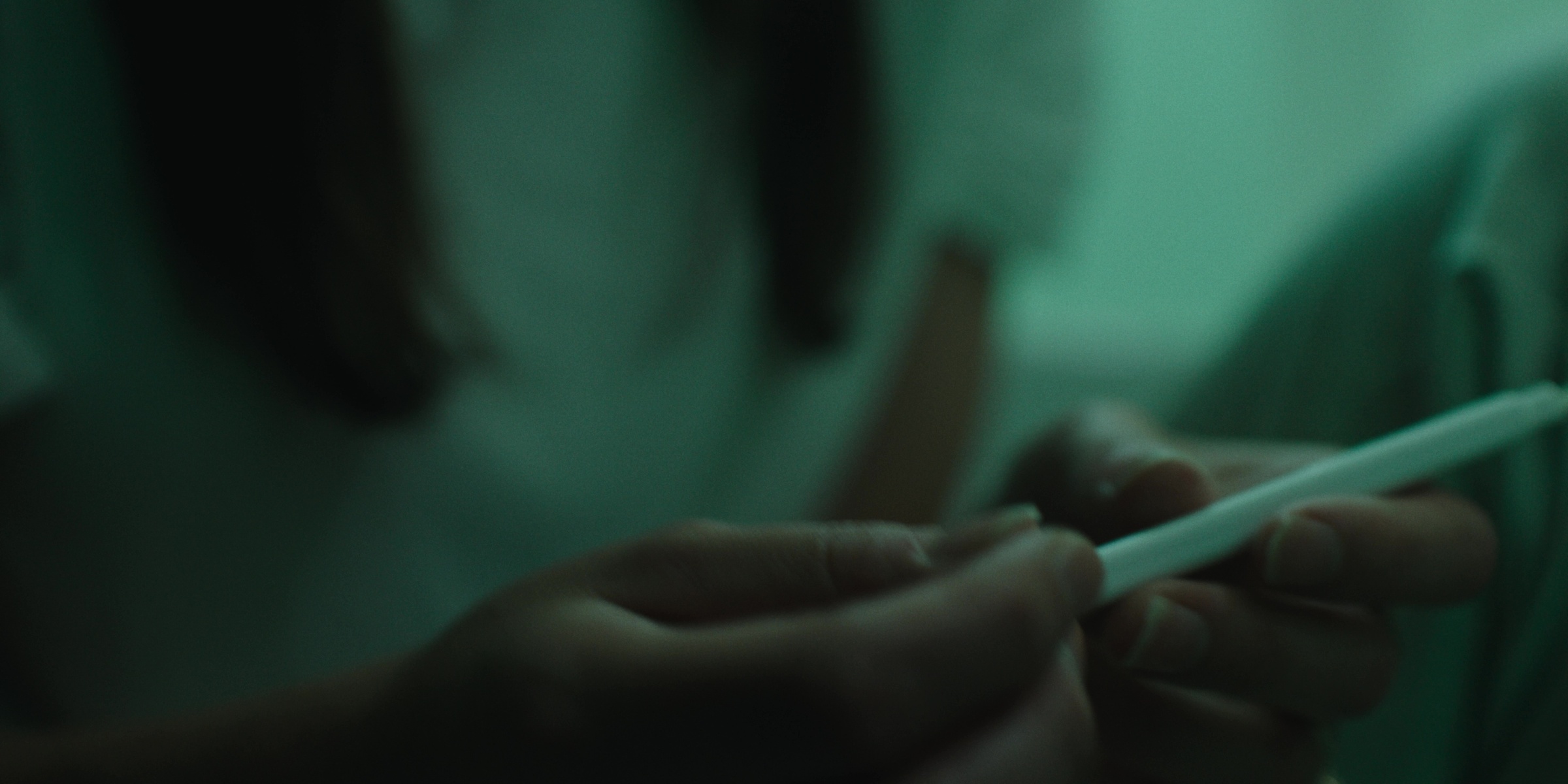 Hands hold a slender white object in cool green light — Bottom of the bottle