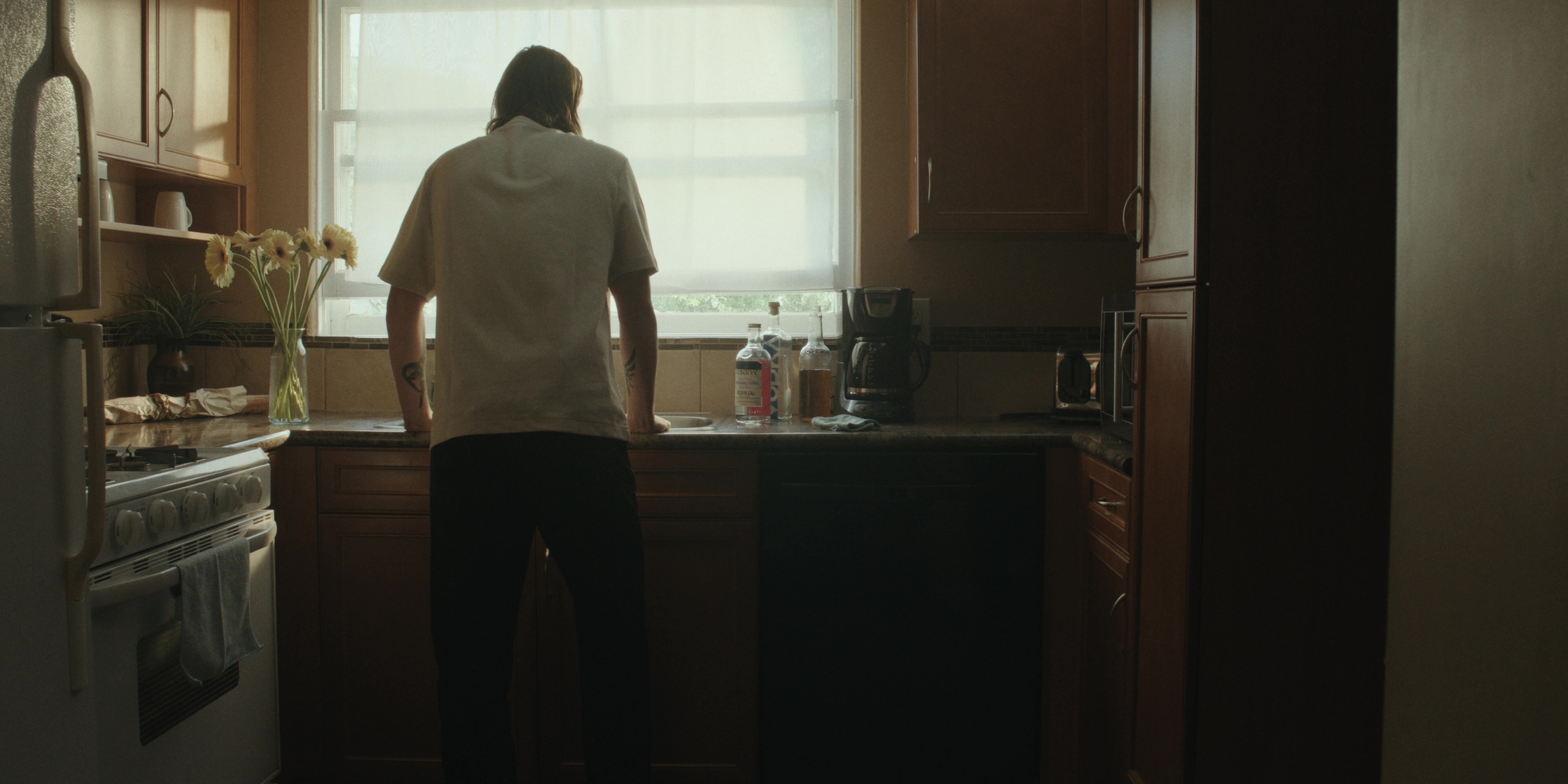 A man stands at the kitchen sink beneath a window — Bottom of the bottle