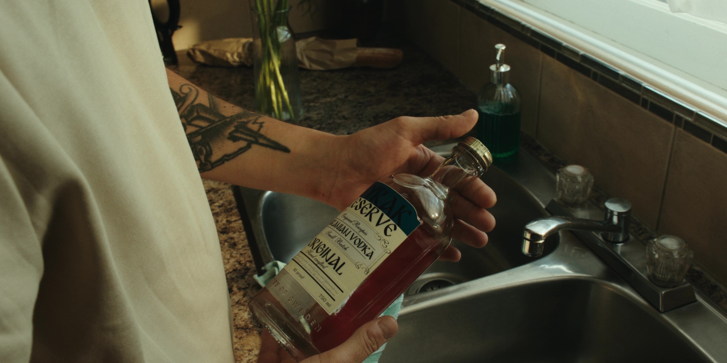 A hand holds a liquor bottle above a kitchen sink — Bottom of the bottle