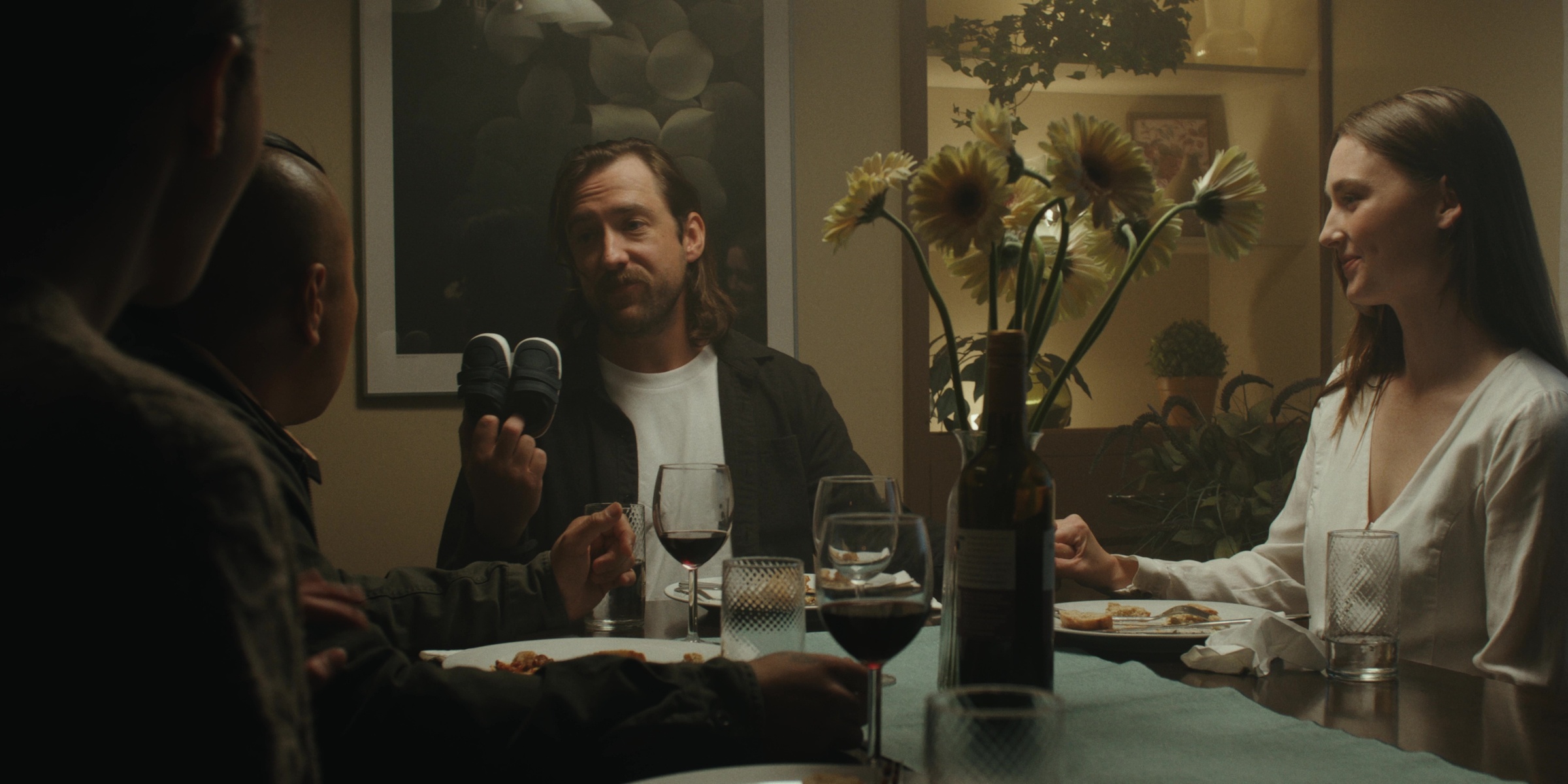 Friends sit around a dinner table with flowers and wine — Bottom of the bottle