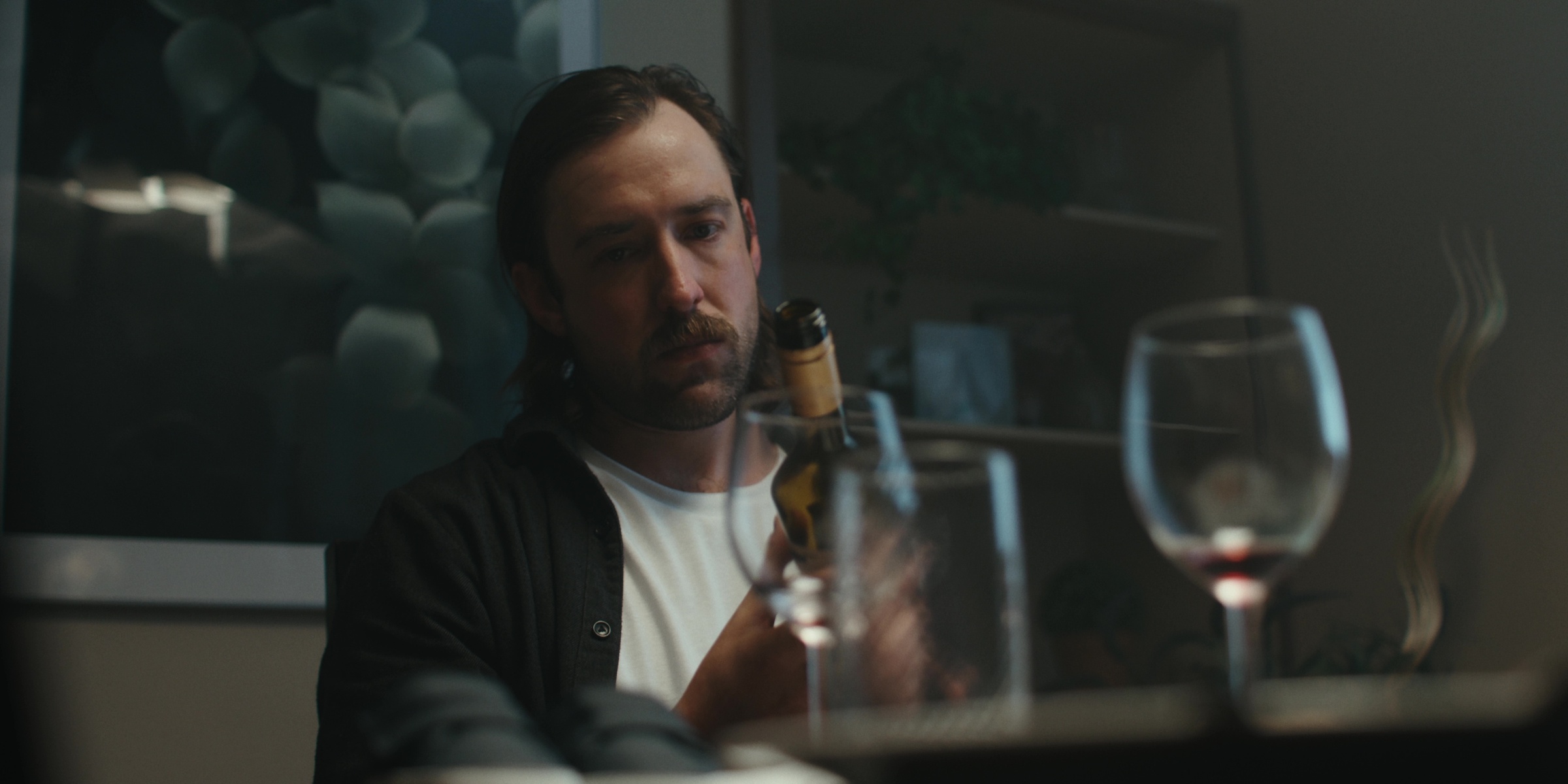 A man looks across a dining table past empty glasses — Bottom of the bottle