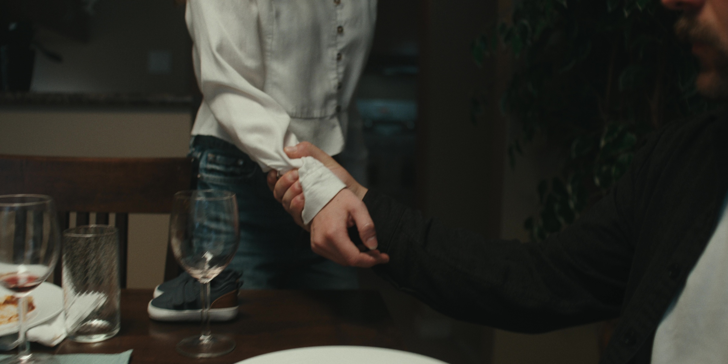 A hand grips a woman’s wrist beside a dinner table — Bottom of the bottle