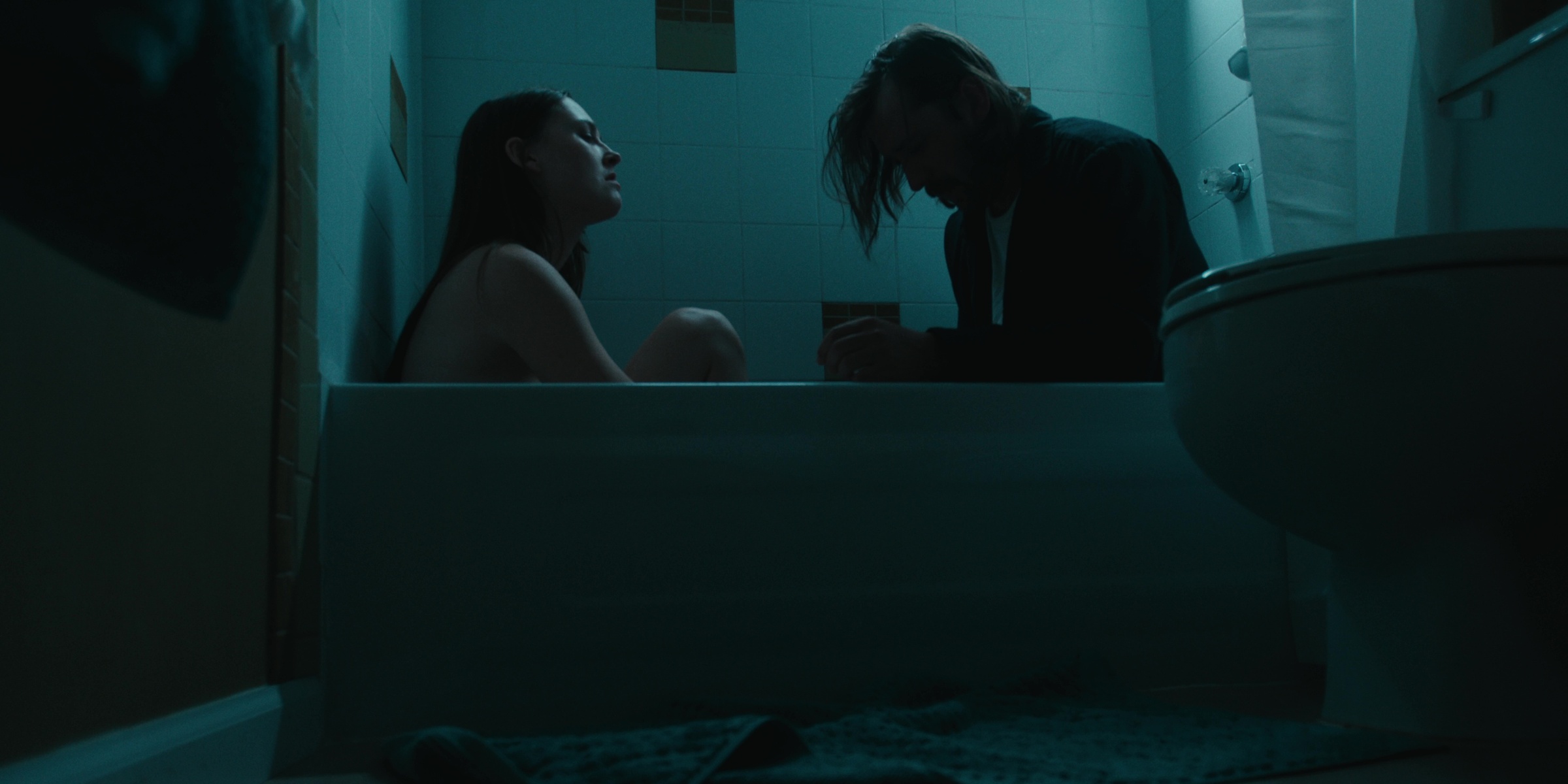 Two people sit beside a bathtub in blue light — Bottom of the bottle