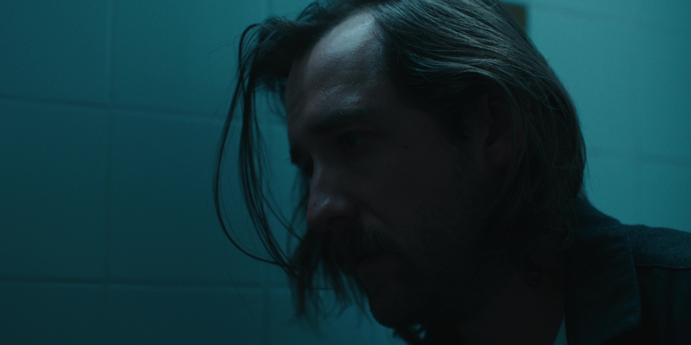 A man looks down in a blue-lit bathroom — Bottom of the bottle