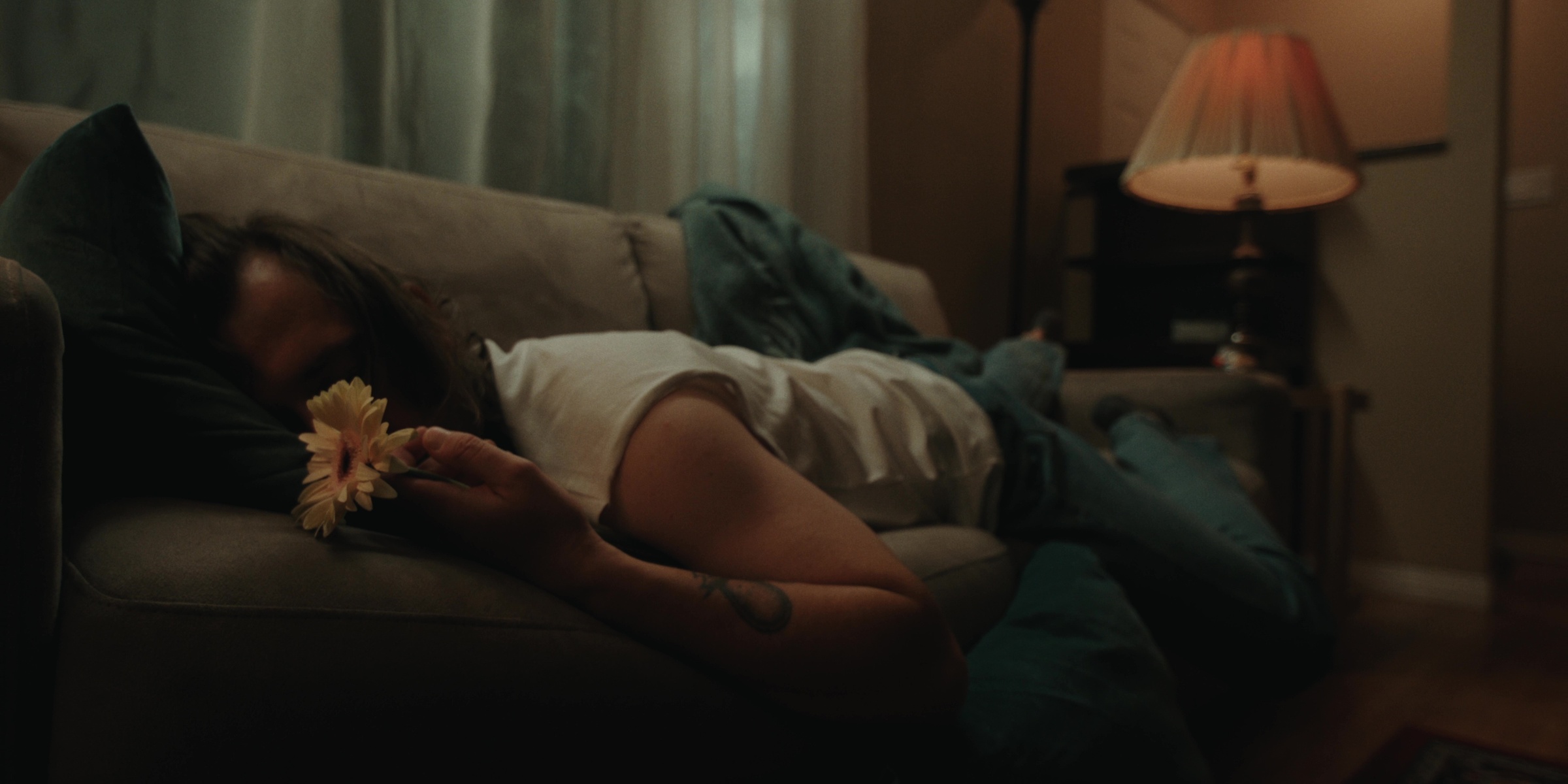 A woman lies on a sofa holding a flower — Bottom of the bottle
