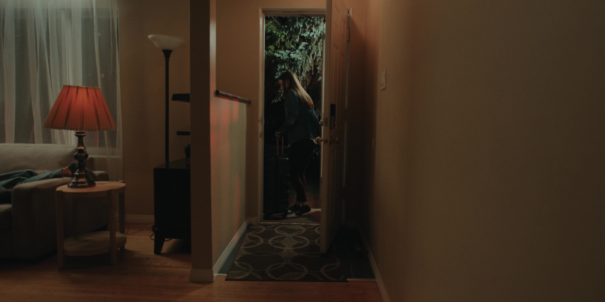 A woman stands at the end of a dim hallway — Bottom of the bottle