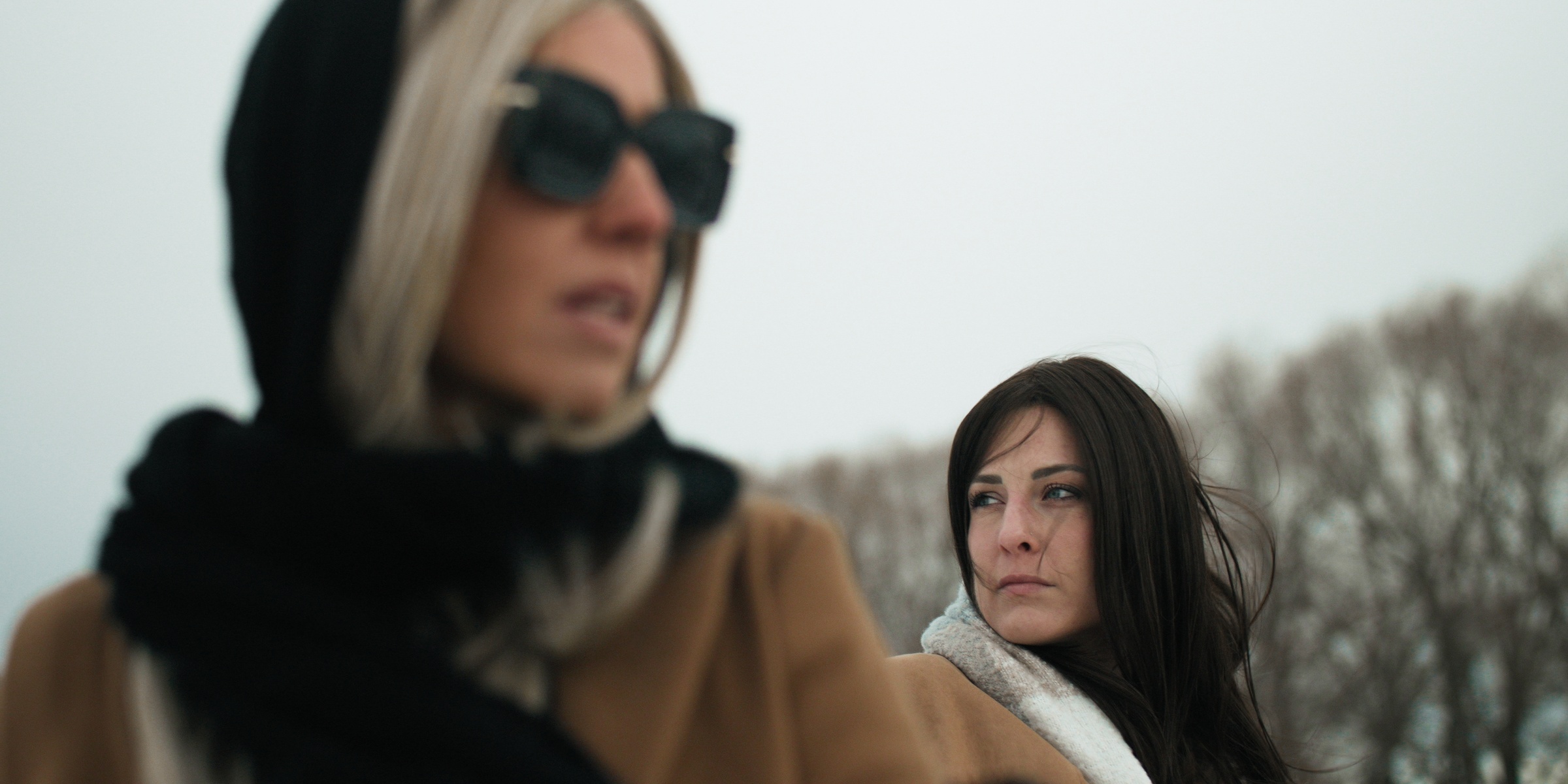 Two women in coats stand outdoors, with sunglasses and a black scarf in the foreground — Chiquel