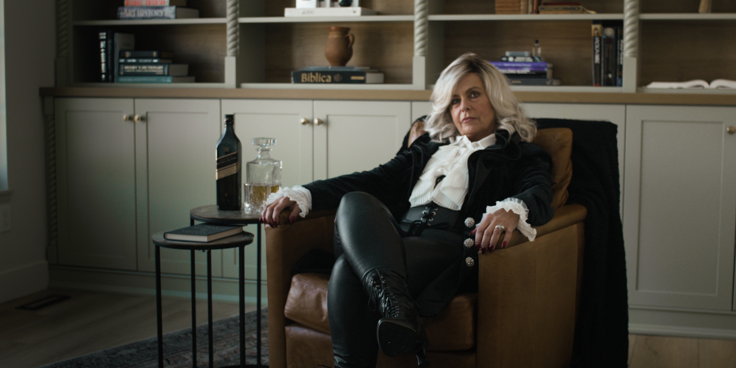 A blonde woman sits in a leather armchair beside a drinks table — Chiquel