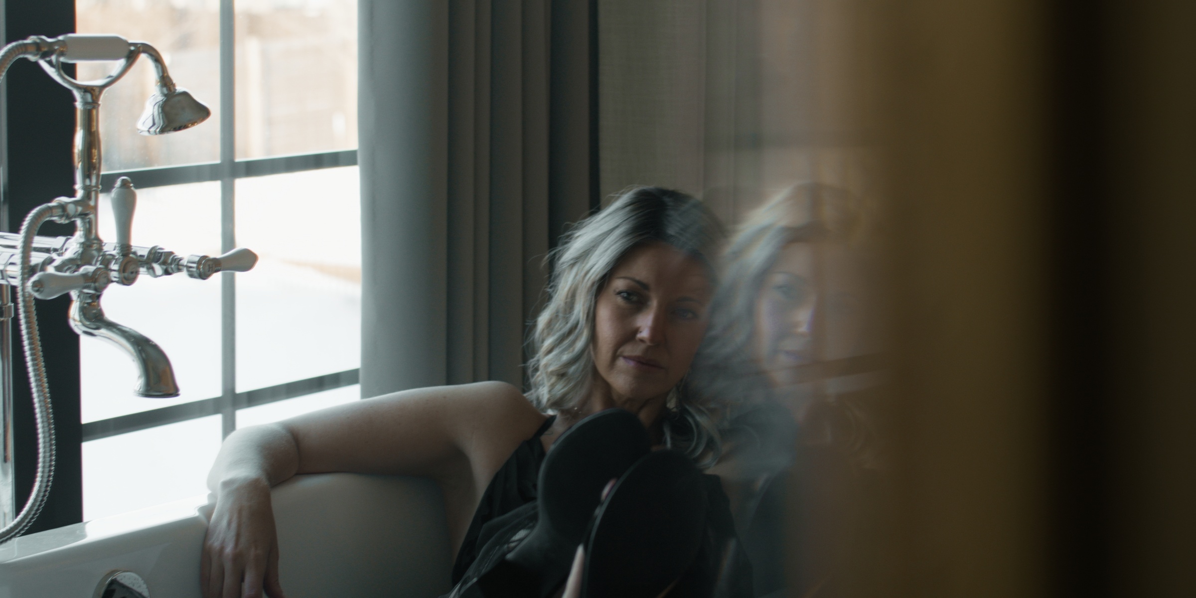 A woman reclines beside a window and a freestanding bath — Chiquel