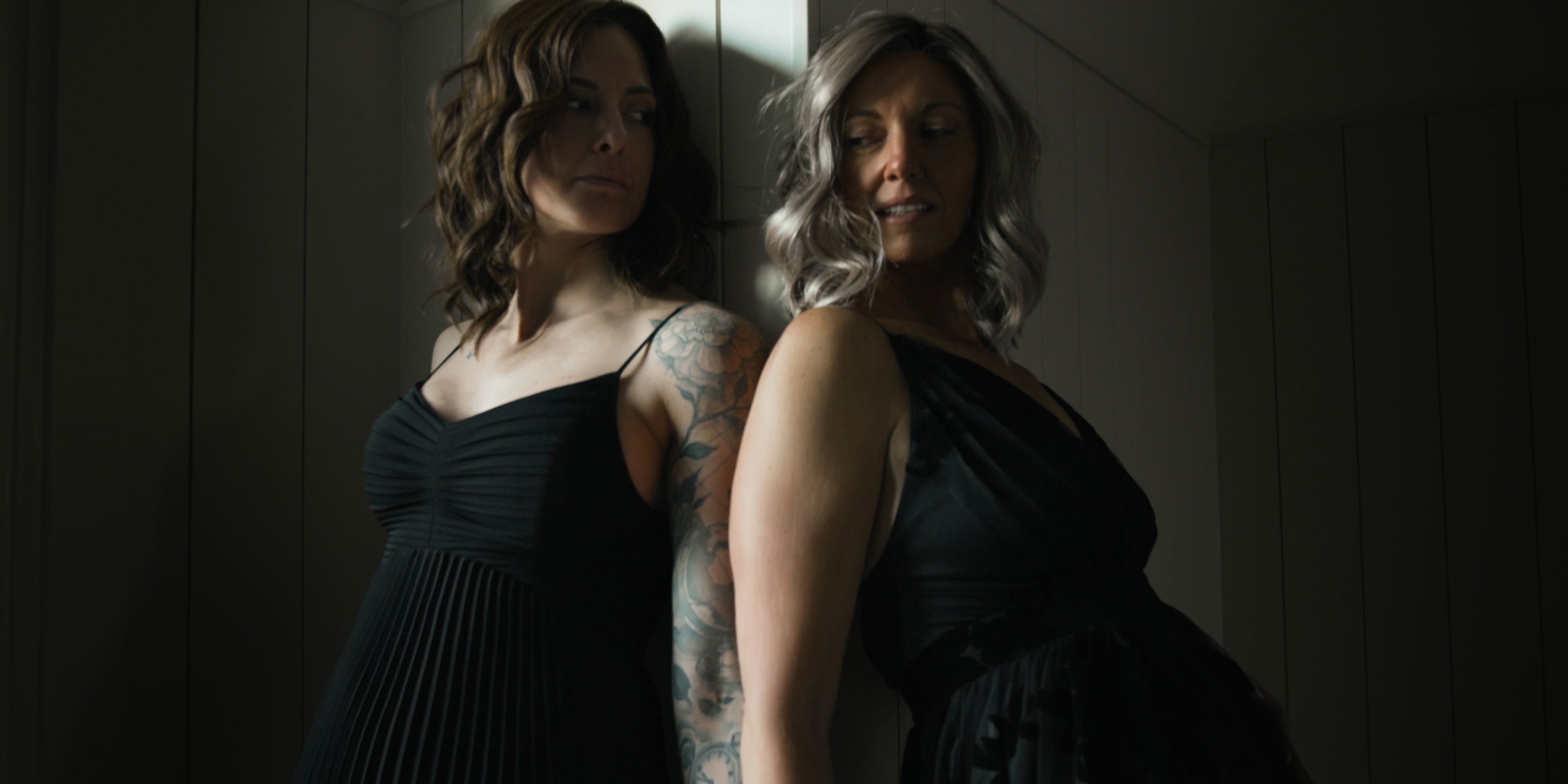 Two women in black dresses stand together in a dim interior — Chiquel