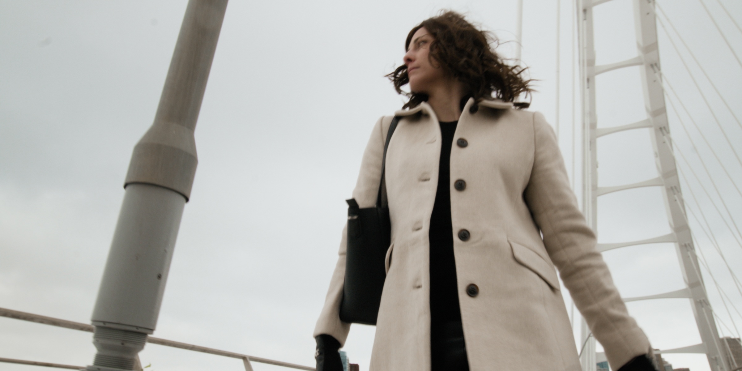 Low-angle view of a woman in a cream coat on a bridge — Chiquel
