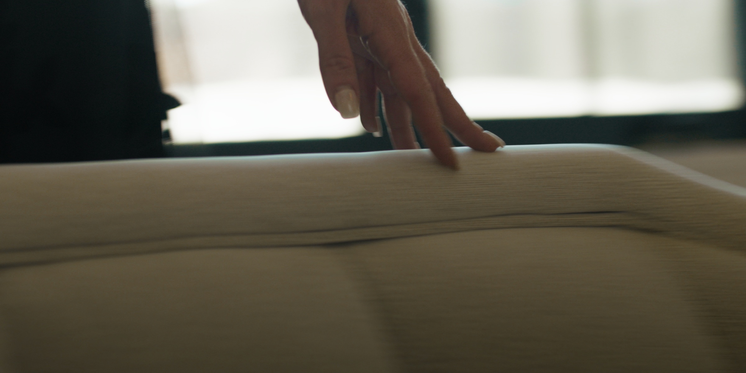 A hand trails across the curved back of an upholstered chair — Chiquel