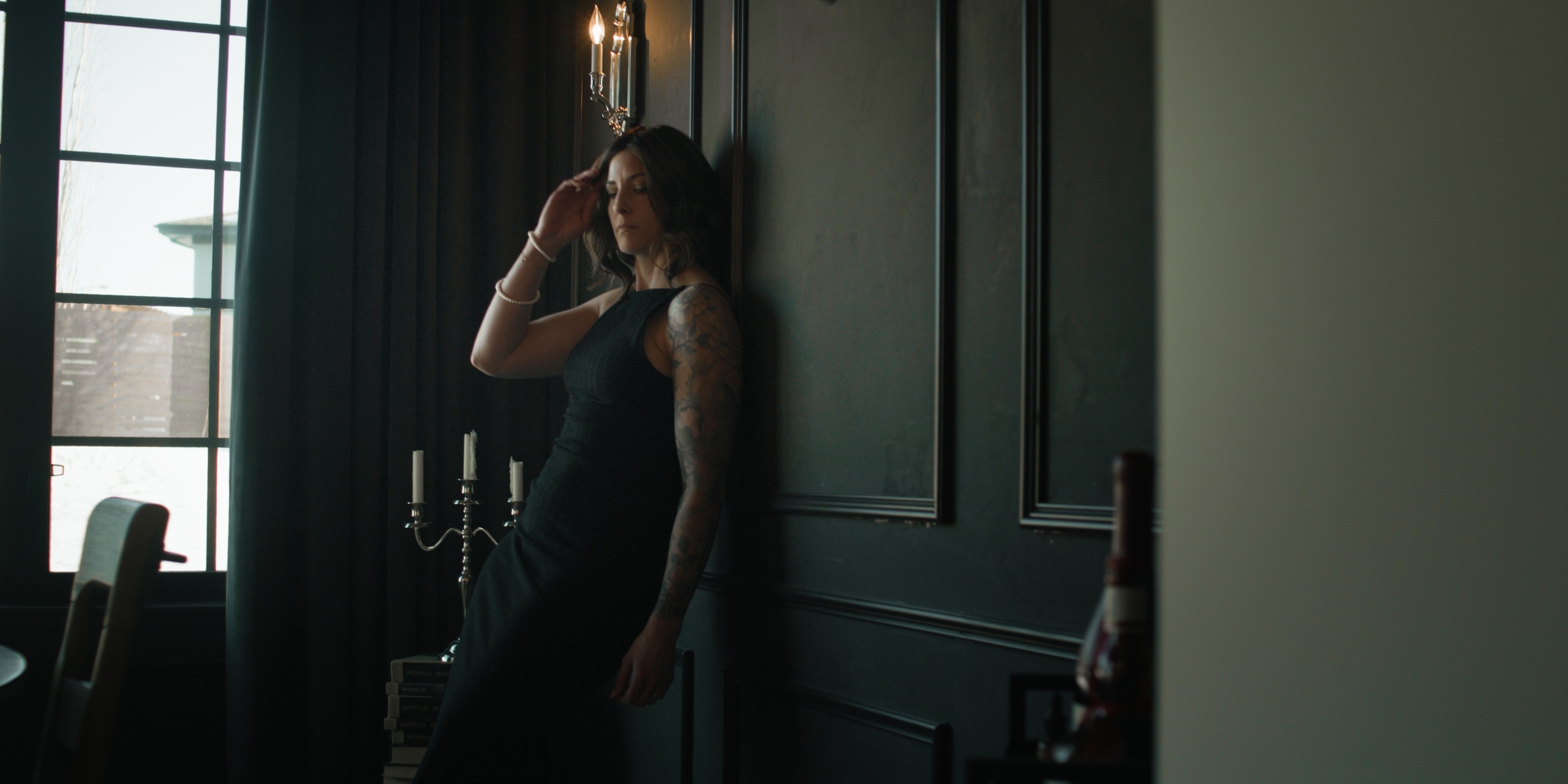 A woman in a black dress leans against a dark paneled wall — Chiquel