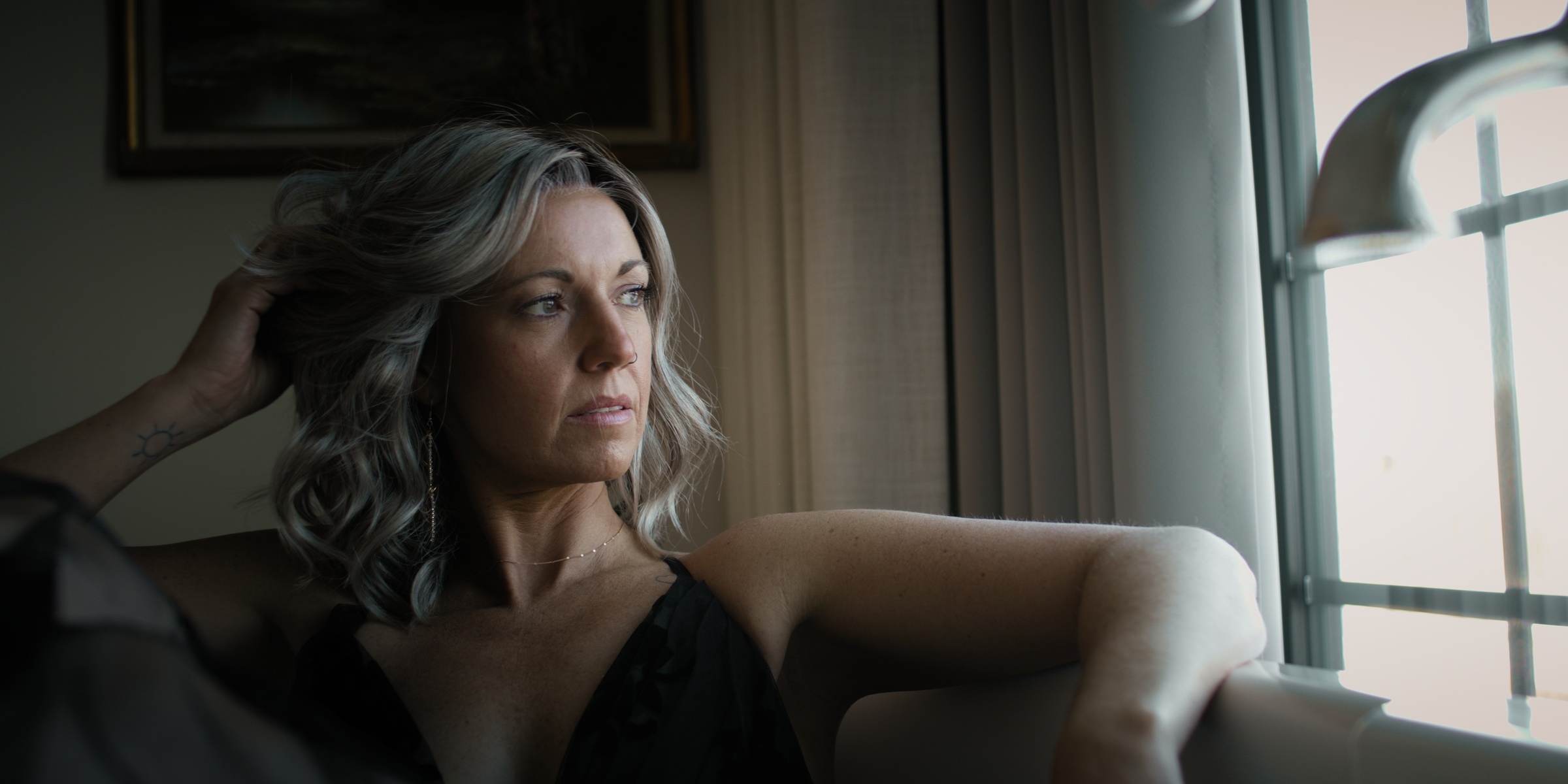 A woman with wavy blonde hair rests beside a bright window — Chiquel