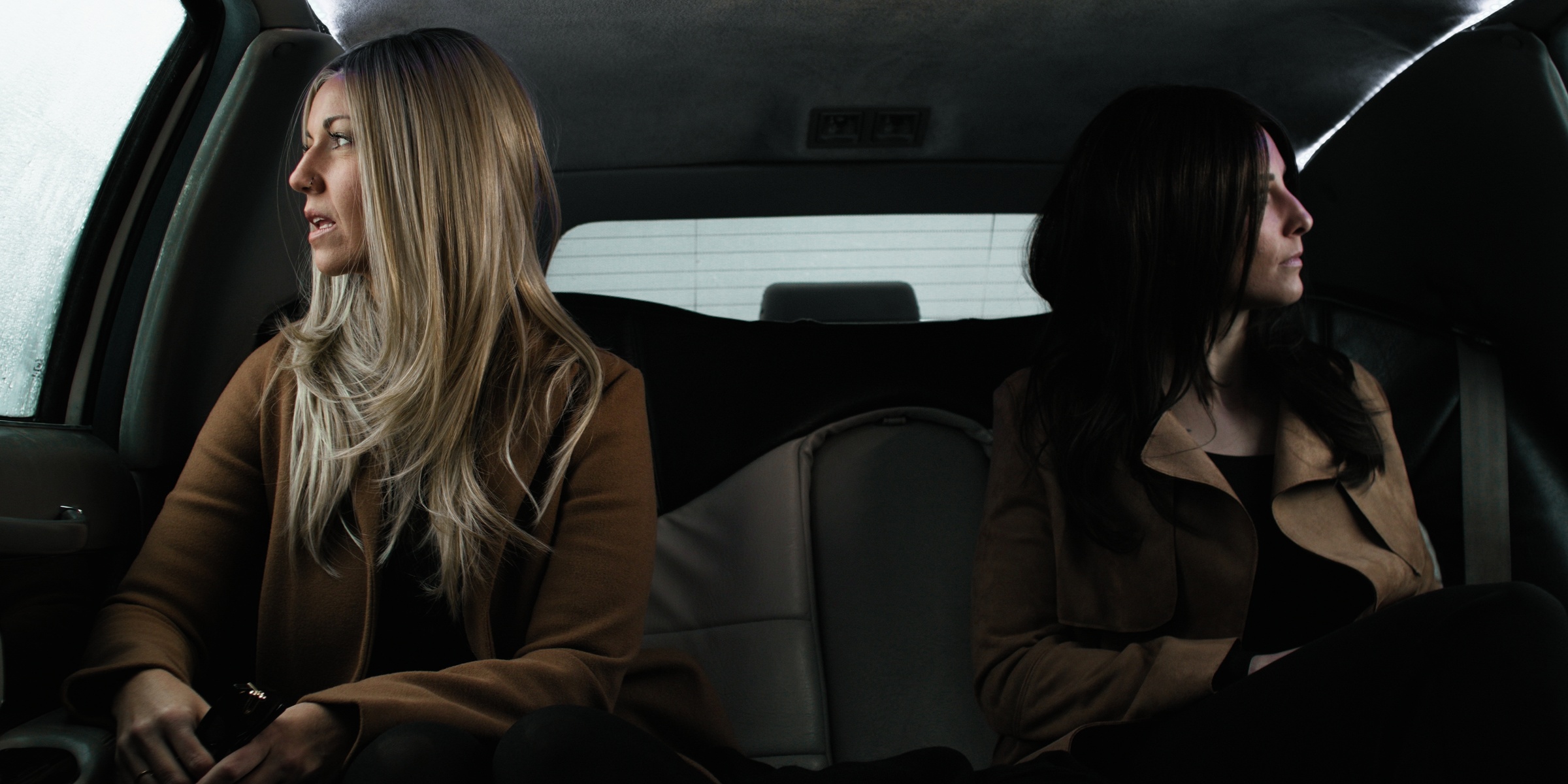 Two women look out opposite windows from the back seat of a car — Chiquel