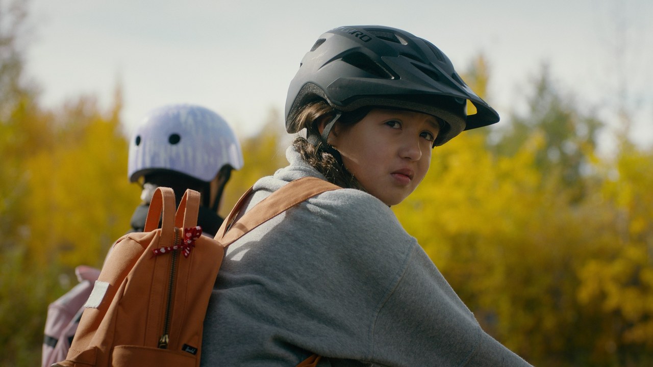 A helmeted child looks back while riding a bicycle beside autumn trees — Communikit