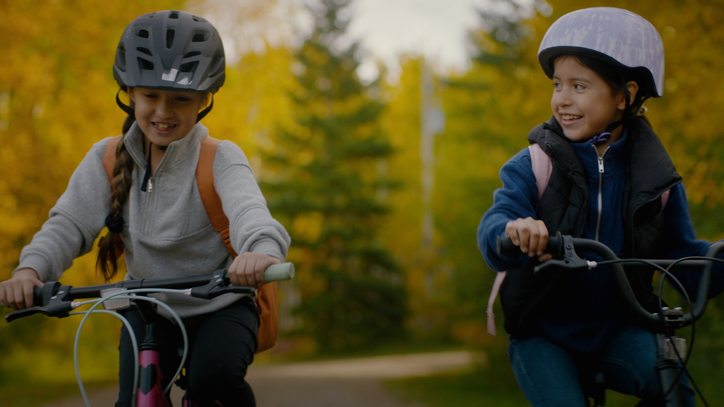 Two helmeted children talk while riding bicycles — Communikit