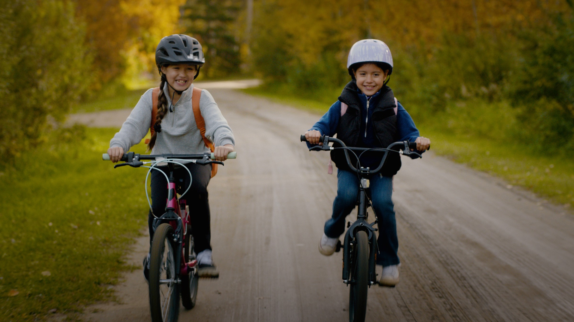 Two children cycle side by side along a rural road — Communikit