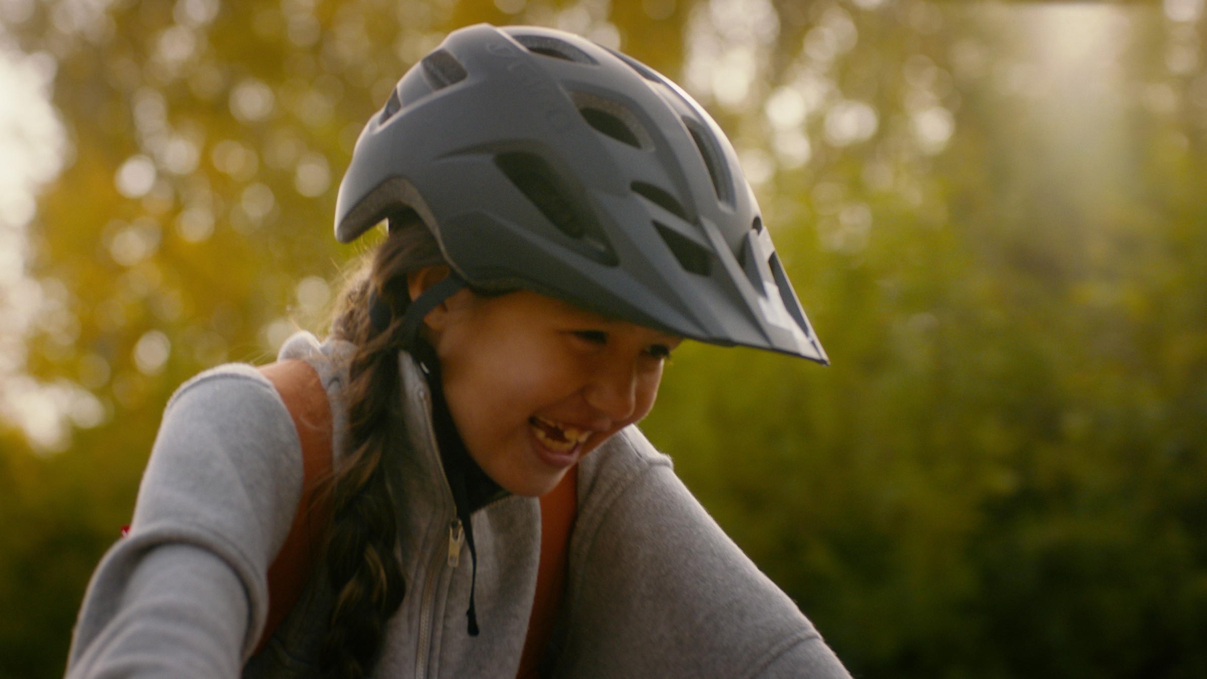 A smiling child wears a bicycle helmet against golden autumn leaves — Communikit