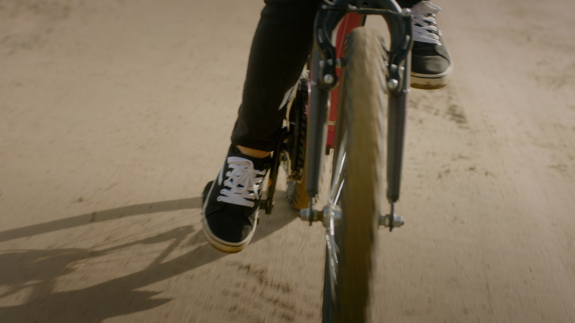 A bicycle wheel and a rider's feet on a sunlit road — Communikit