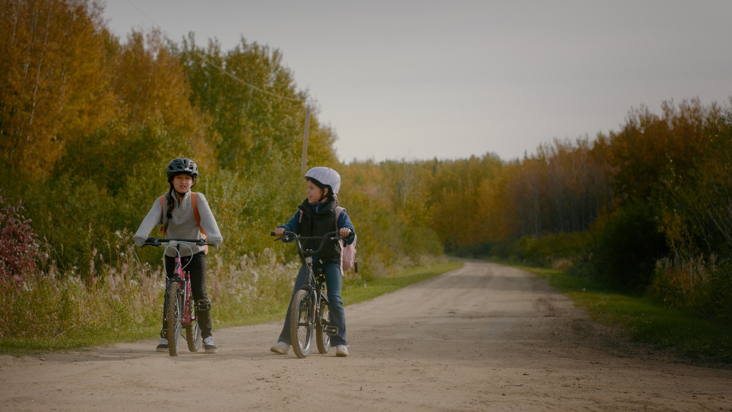 Two children ride bicycles along a tree-lined gravel road — Communikit