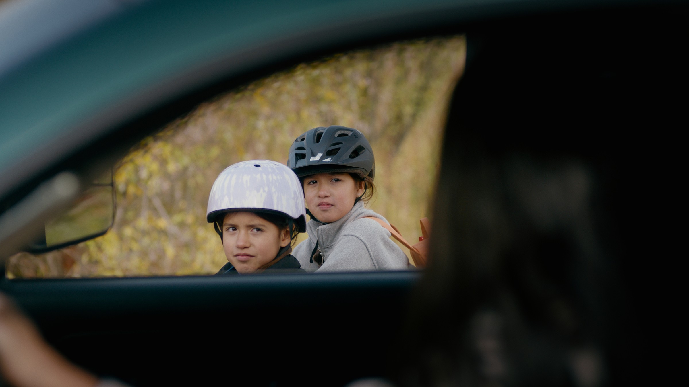 Two children with bicycle helmets seen through a car window — Communikit
