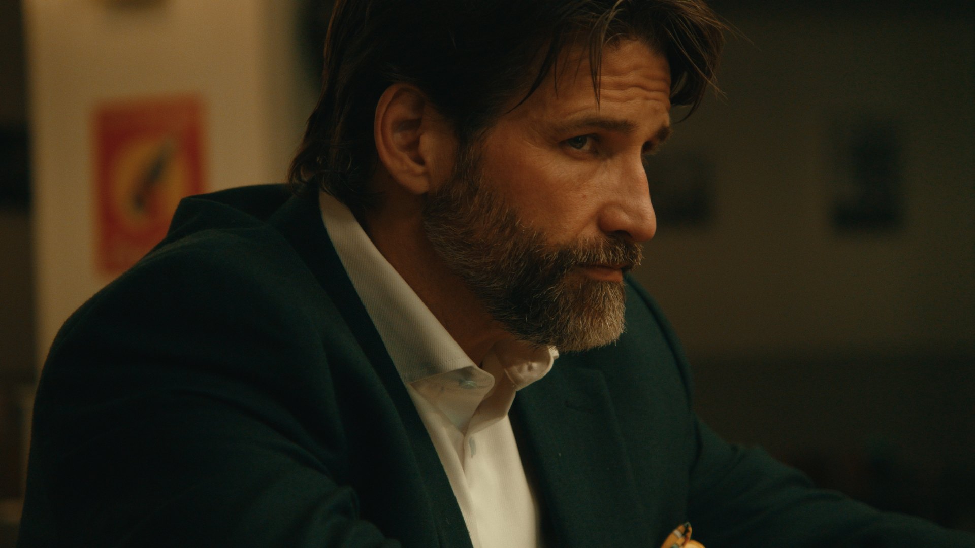 A bearded man in a dark suit under warm interior light — Crossroads