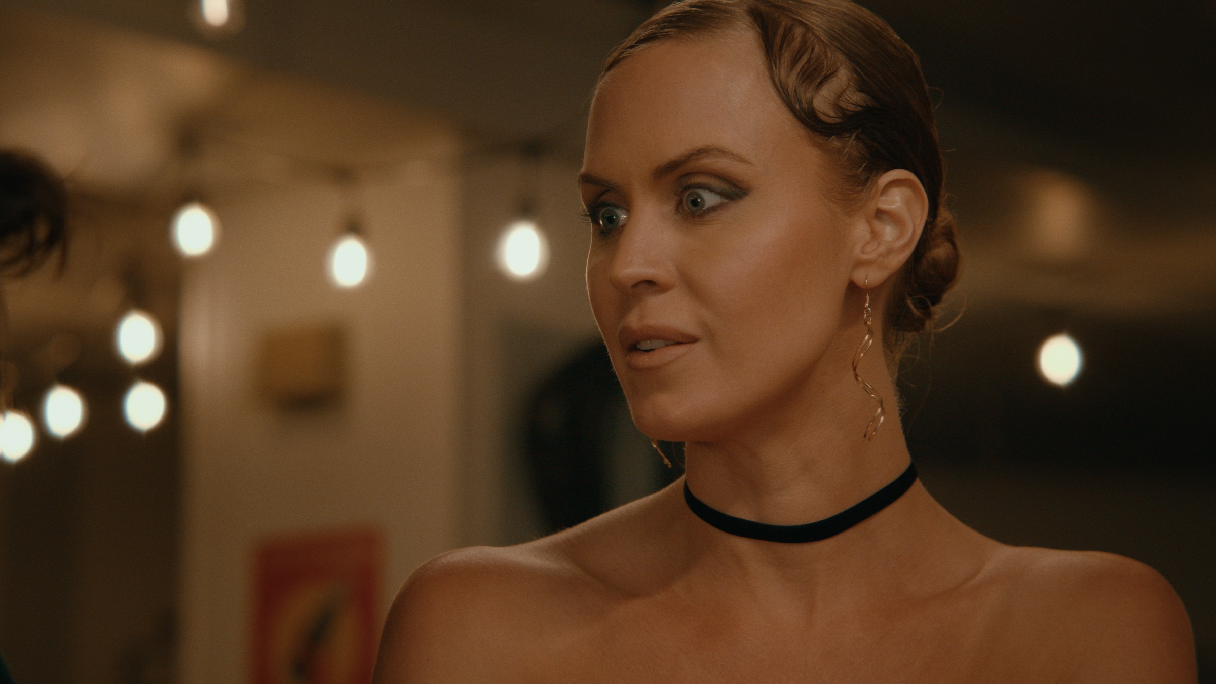 A woman wearing a black choker looks to the side under warm lights — Crossroads