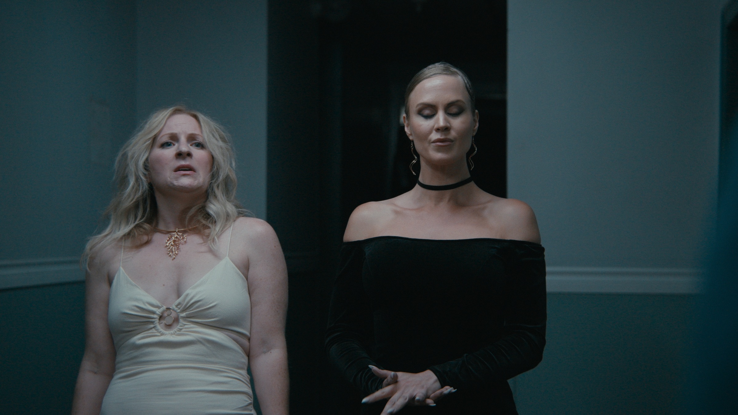 Two women stand together in a cool blue hallway — Crossroads