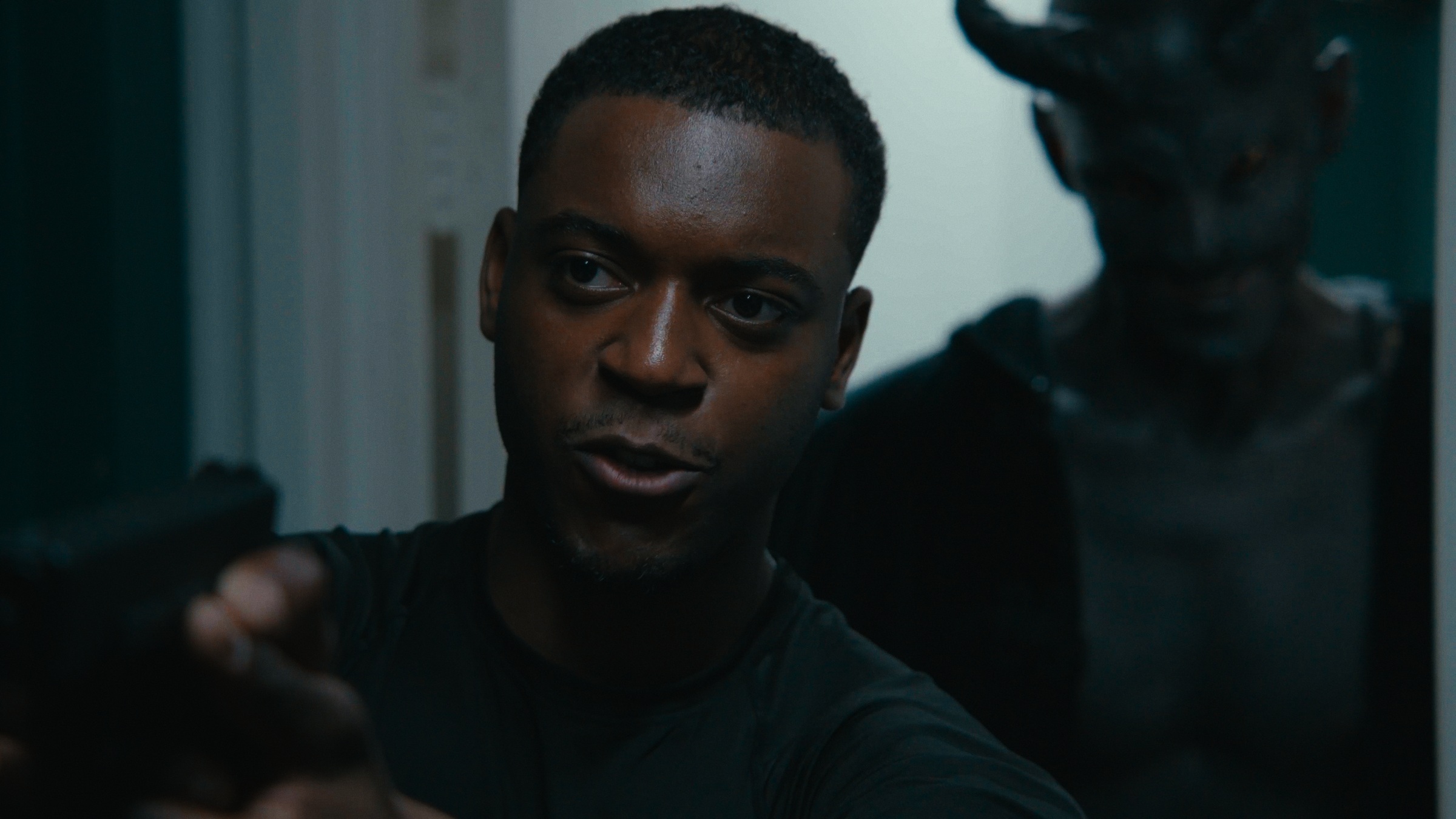 A man in a black shirt points a handgun down a dim hallway — Crossroads