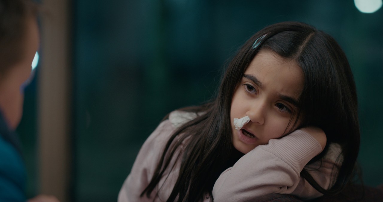 A girl in a pale pink coat rests her chin on her arm in a waiting room — Emergency