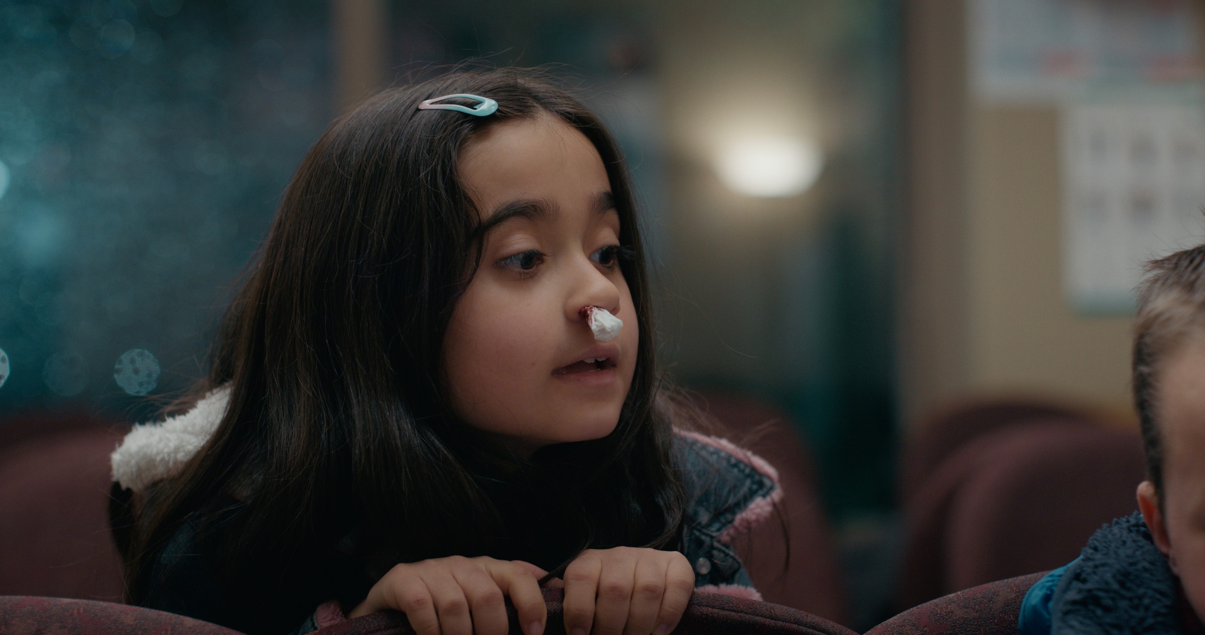 A girl talks across a waiting-room chair — Emergency