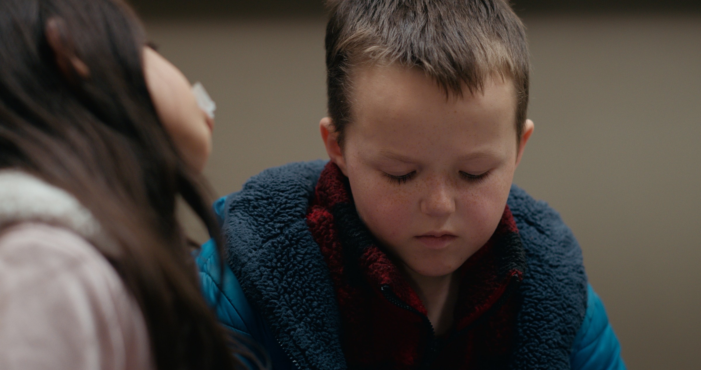 A boy looks down while seated in a waiting room — Emergency