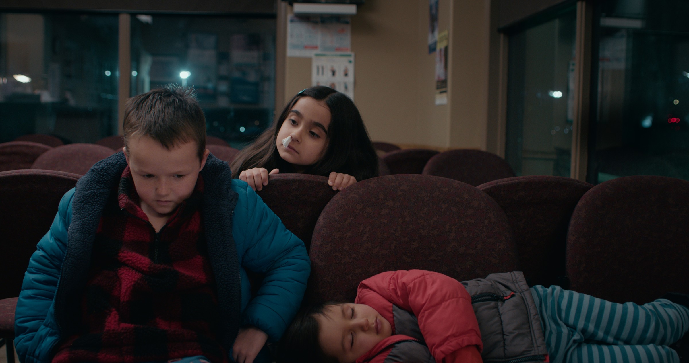A boy in a blue coat leans forward while a girl watches behind him — Emergency