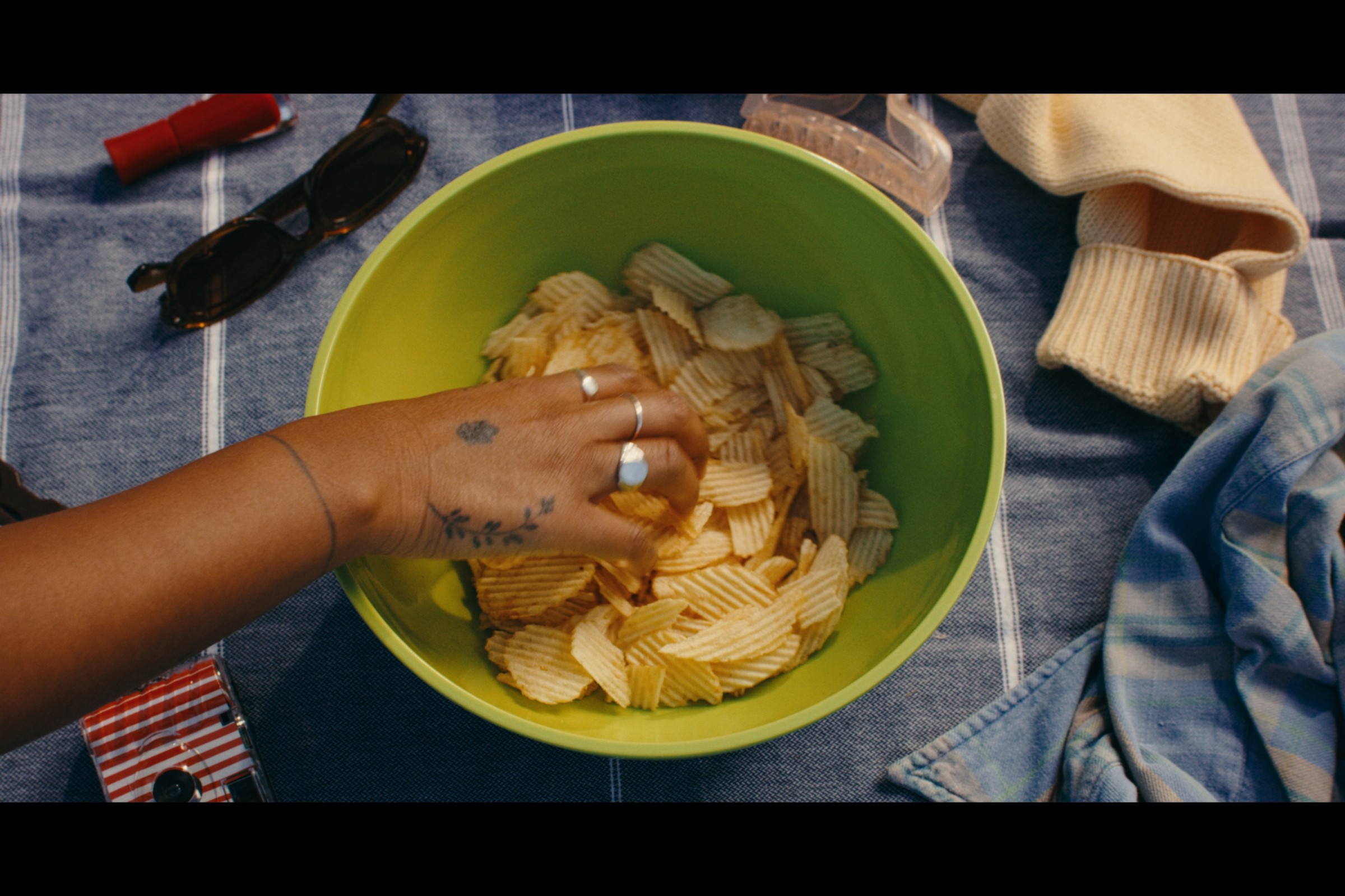 A hand reaches into a bowl of chips at a lakeside picnic — Girls Weekend