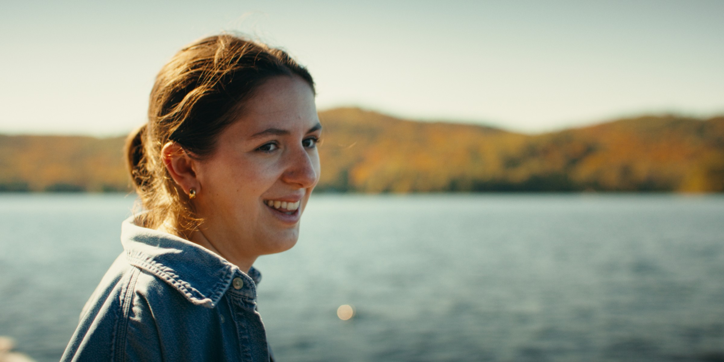 A smiling woman sits beside the lake in warm sunlight — Girls Weekend