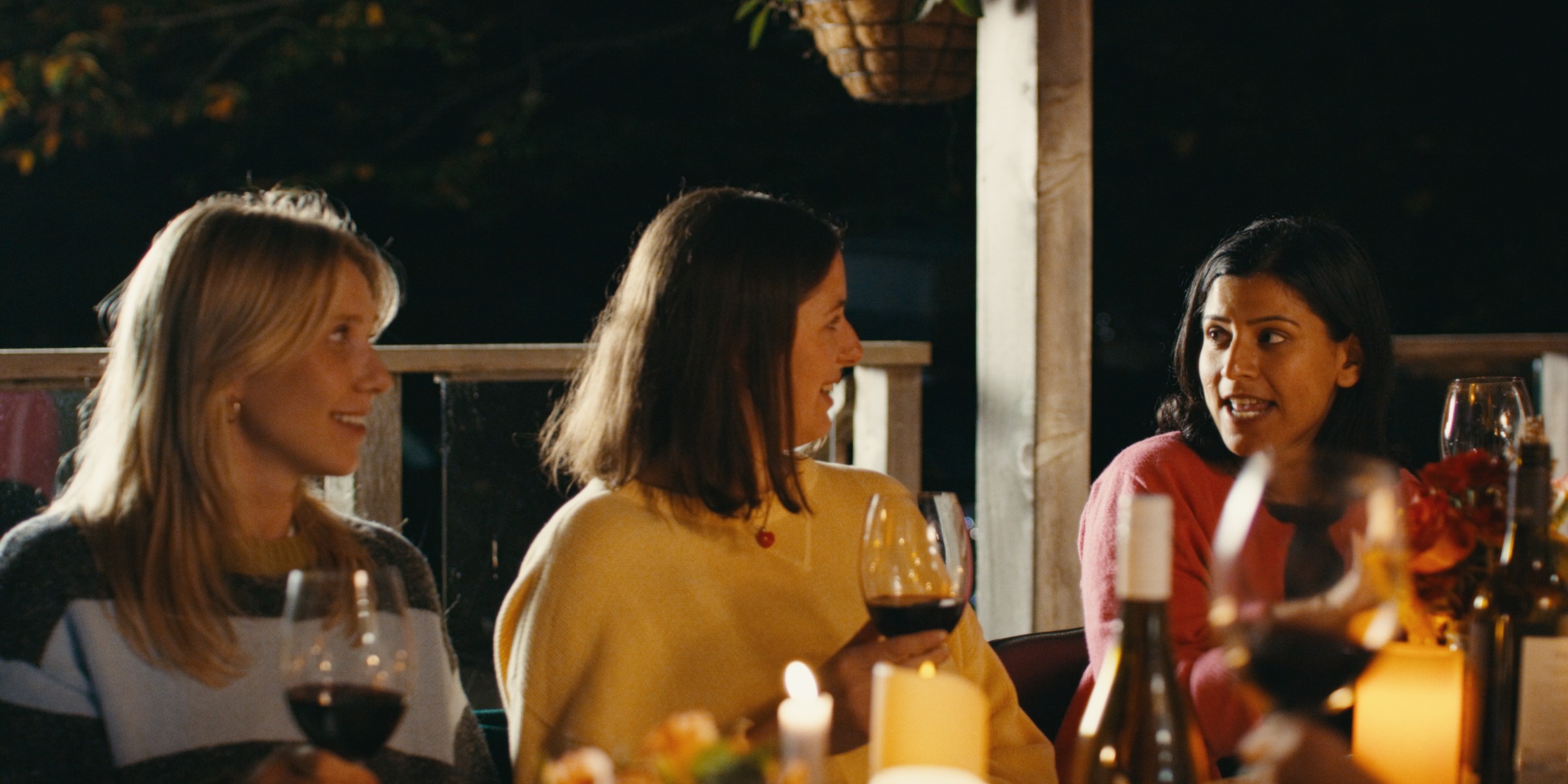 Friends talk around a warmly lit dining table — Girls Weekend