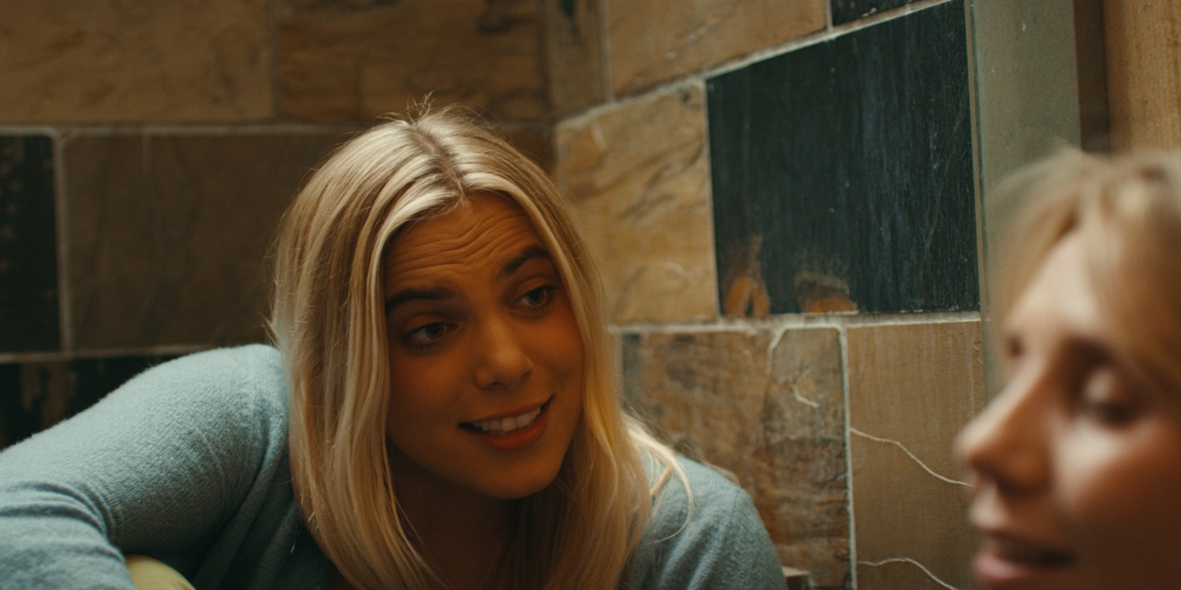A blonde woman talks beside a stone fireplace — Girls Weekend