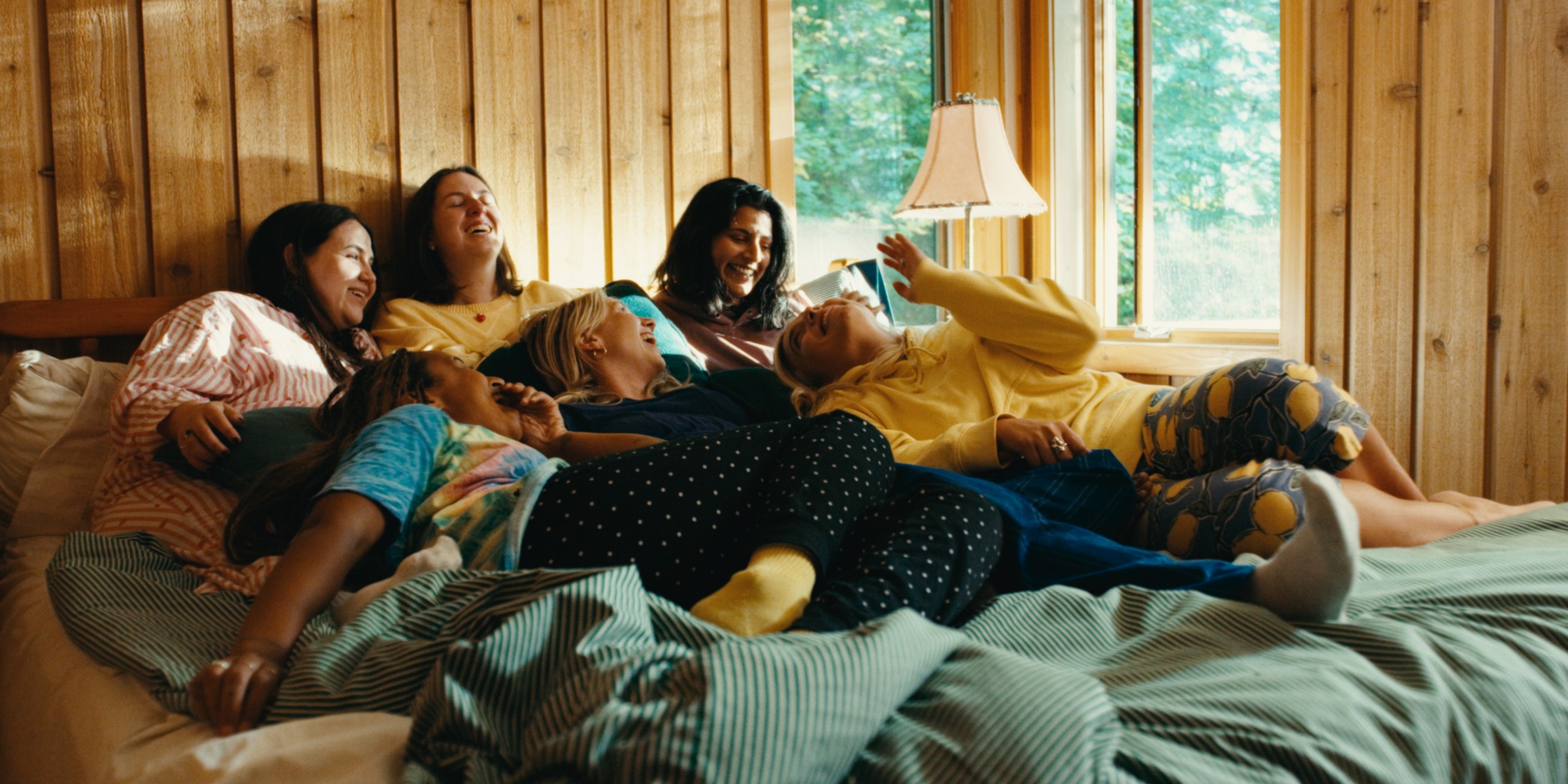 Friends lounge together on a bed in a wood-paneled room — Girls Weekend