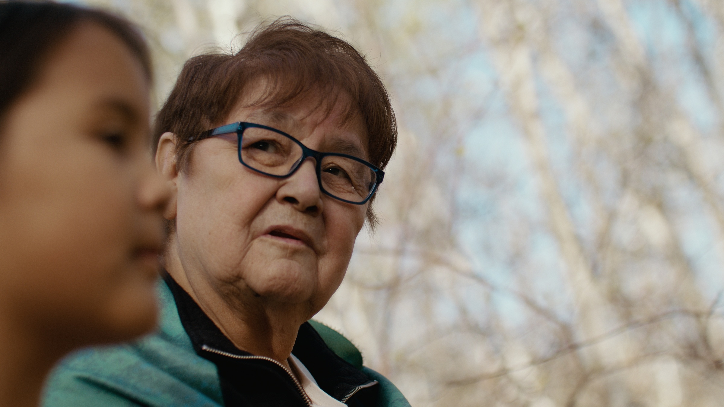 A woman wearing glasses looks toward a child in the woods — Home Fire