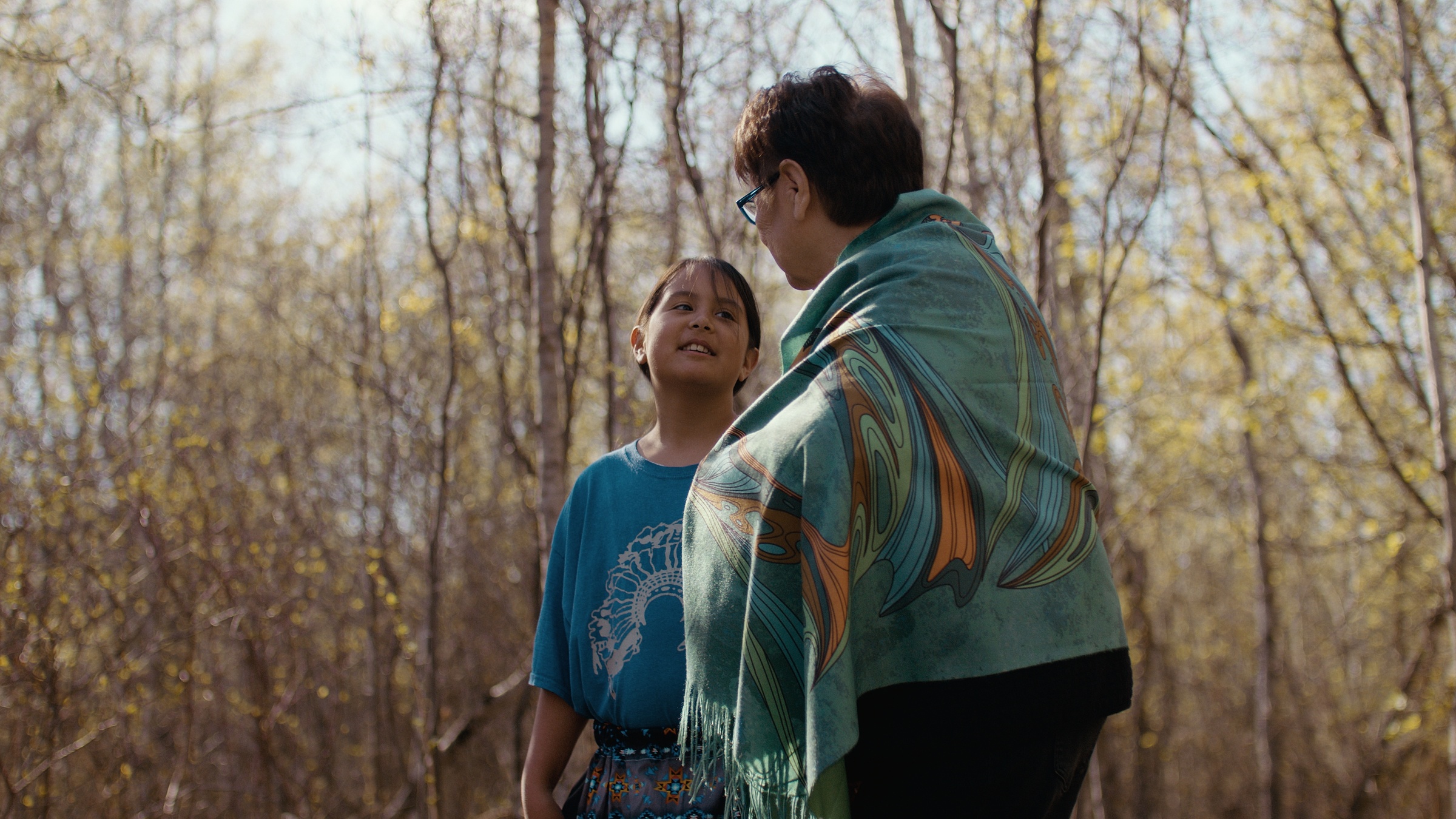 A child smiles up at a woman among sunlit trees — Home Fire