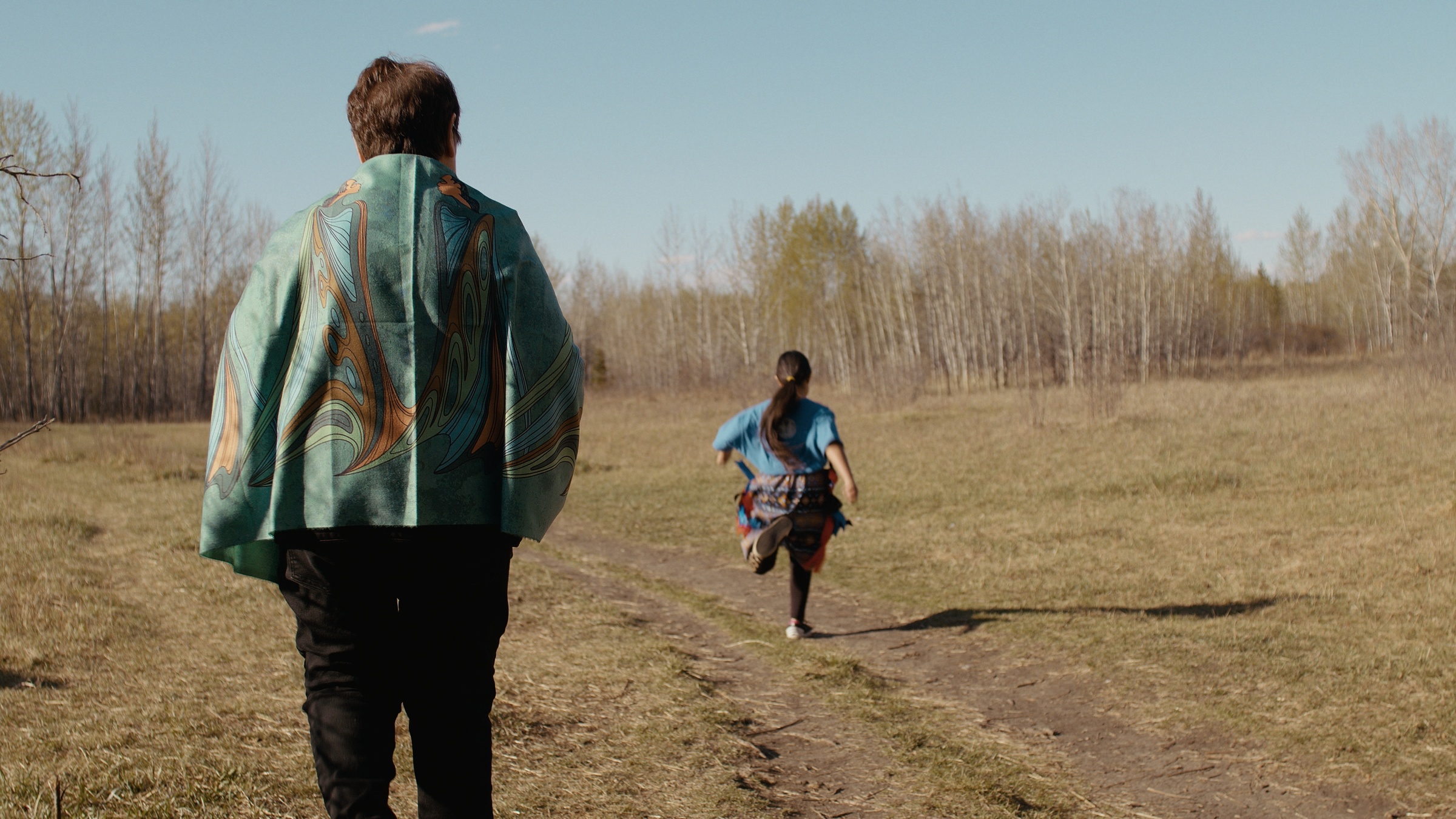 A child runs across a grassy clearing ahead of a woman — Home Fire