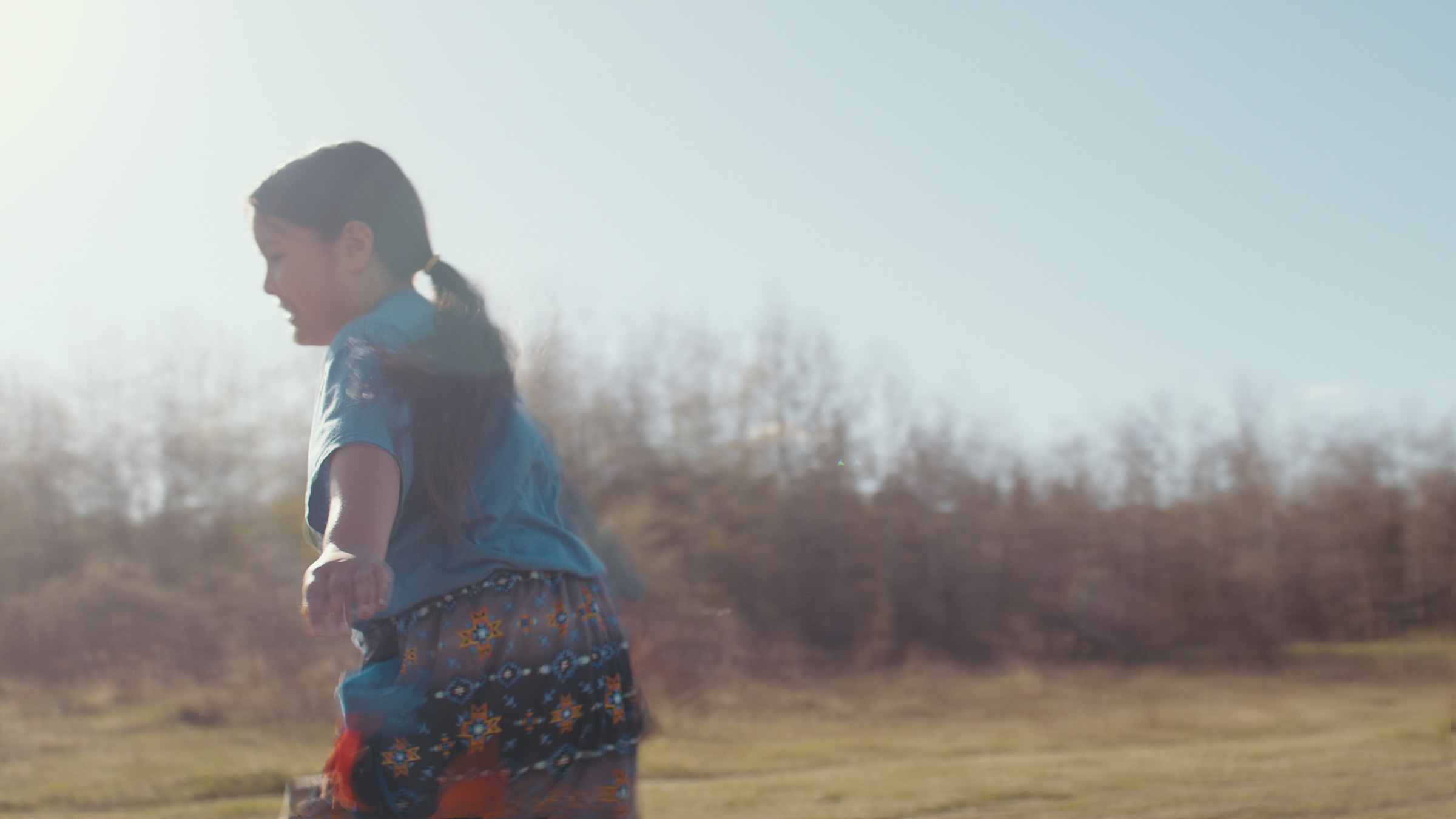 A child in a blue shirt walks across a sunlit clearing — Home Fire