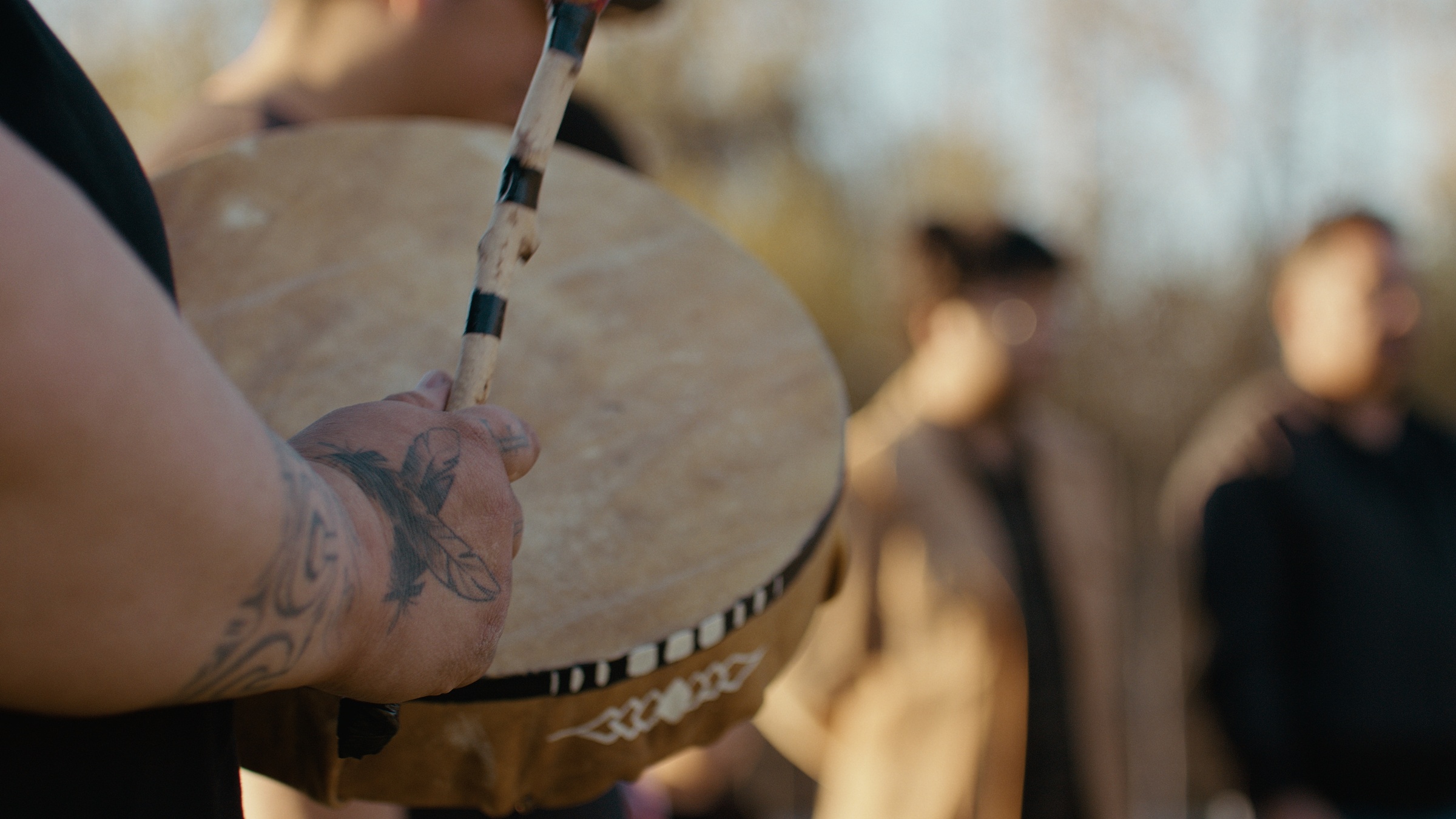 A person holds a drum and beater with a group beyond — Home Fire