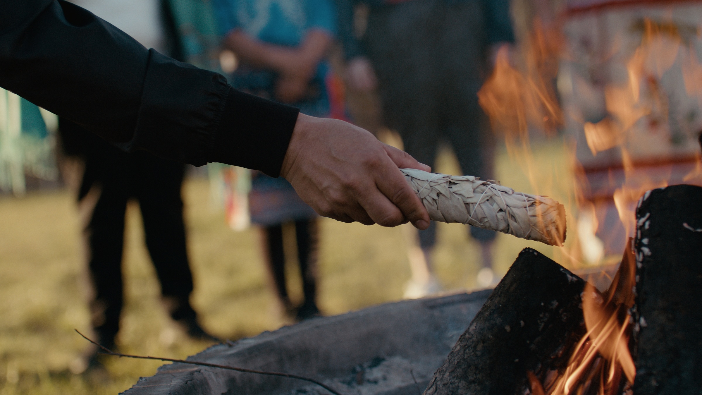 A hand holds a wrapped bundle beside an open fire — Home Fire
