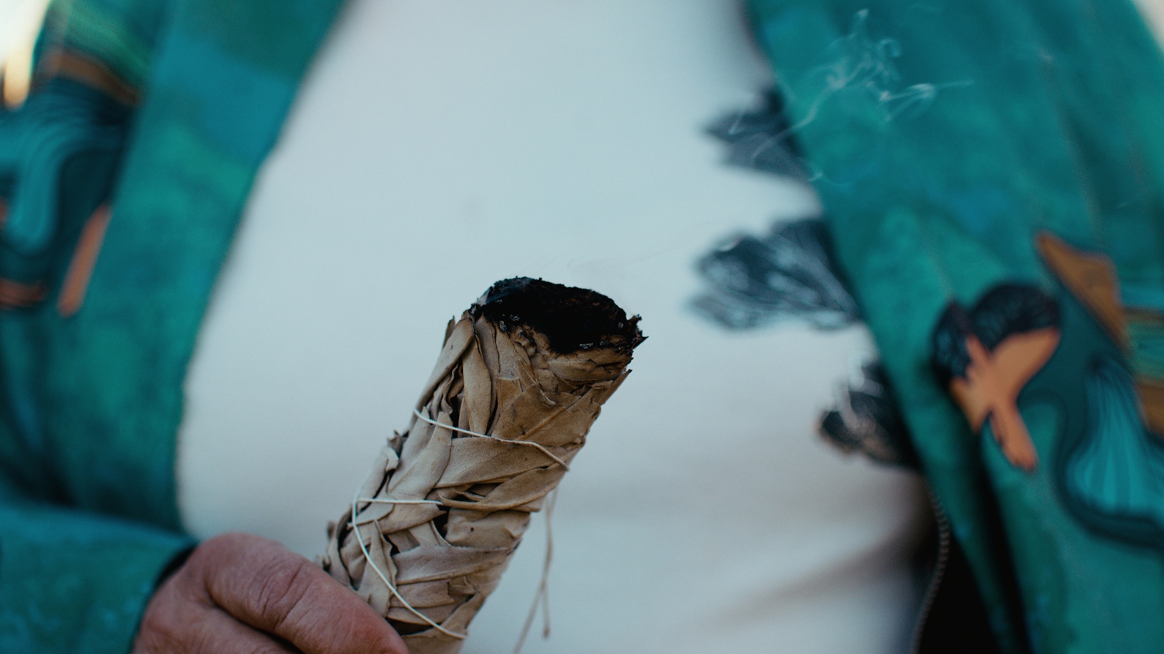 Smoke rises from a wrapped bundle held against a turquoise garment — Home Fire