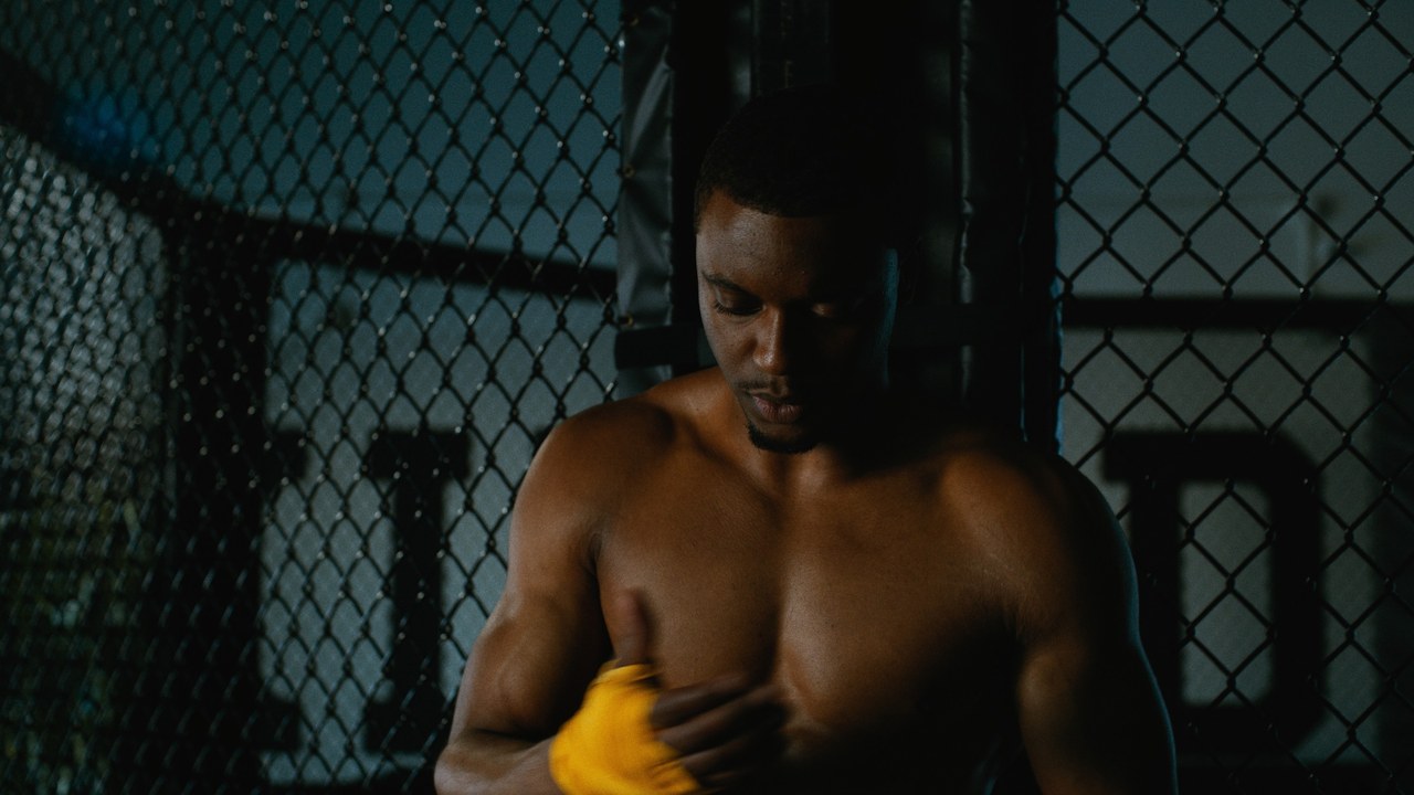 A boxer wraps his hands beside a chain-link training cage — Kinetic